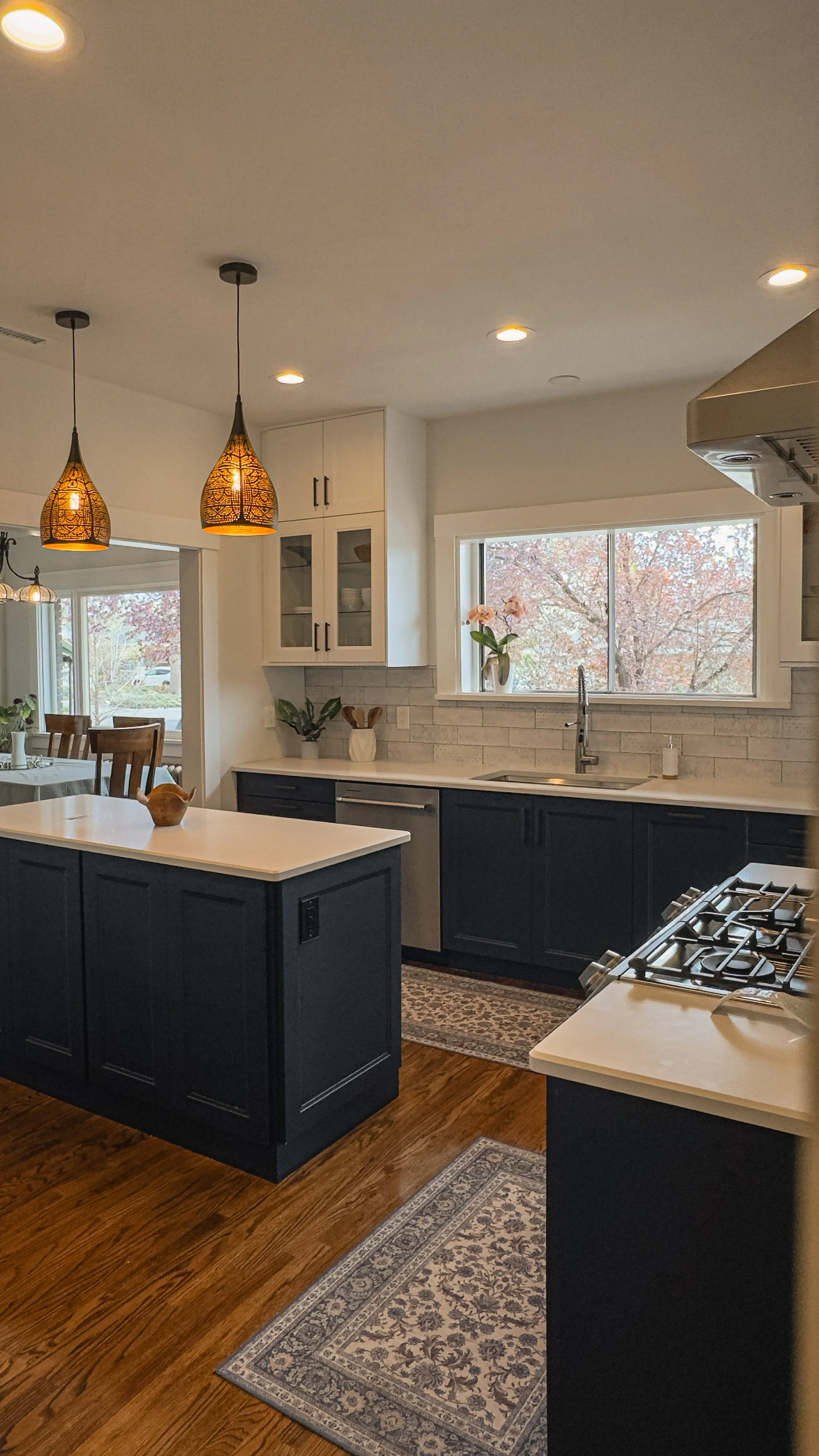 Kitchen with dark island cabinetry, white countertops, pendant lighting, tiled backsplash, and large window in the Emerson residence.