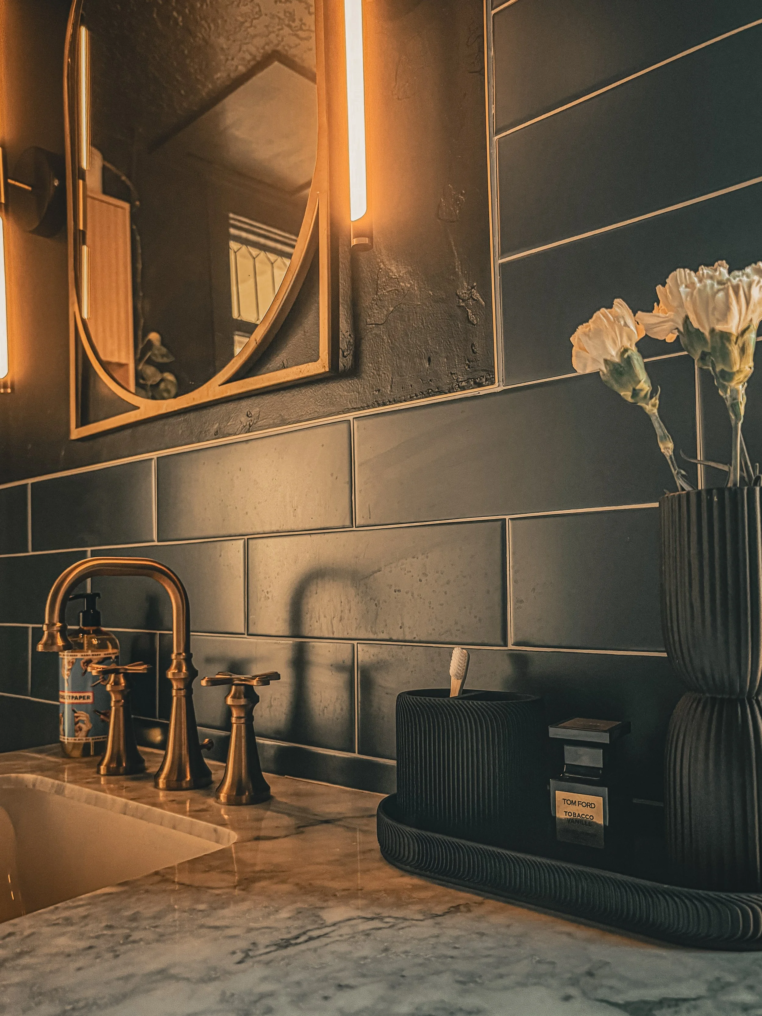 Interior detail at the West Temple residence with dark tile, brass plumbing fixtures, sculptural objects, and warm directional light.