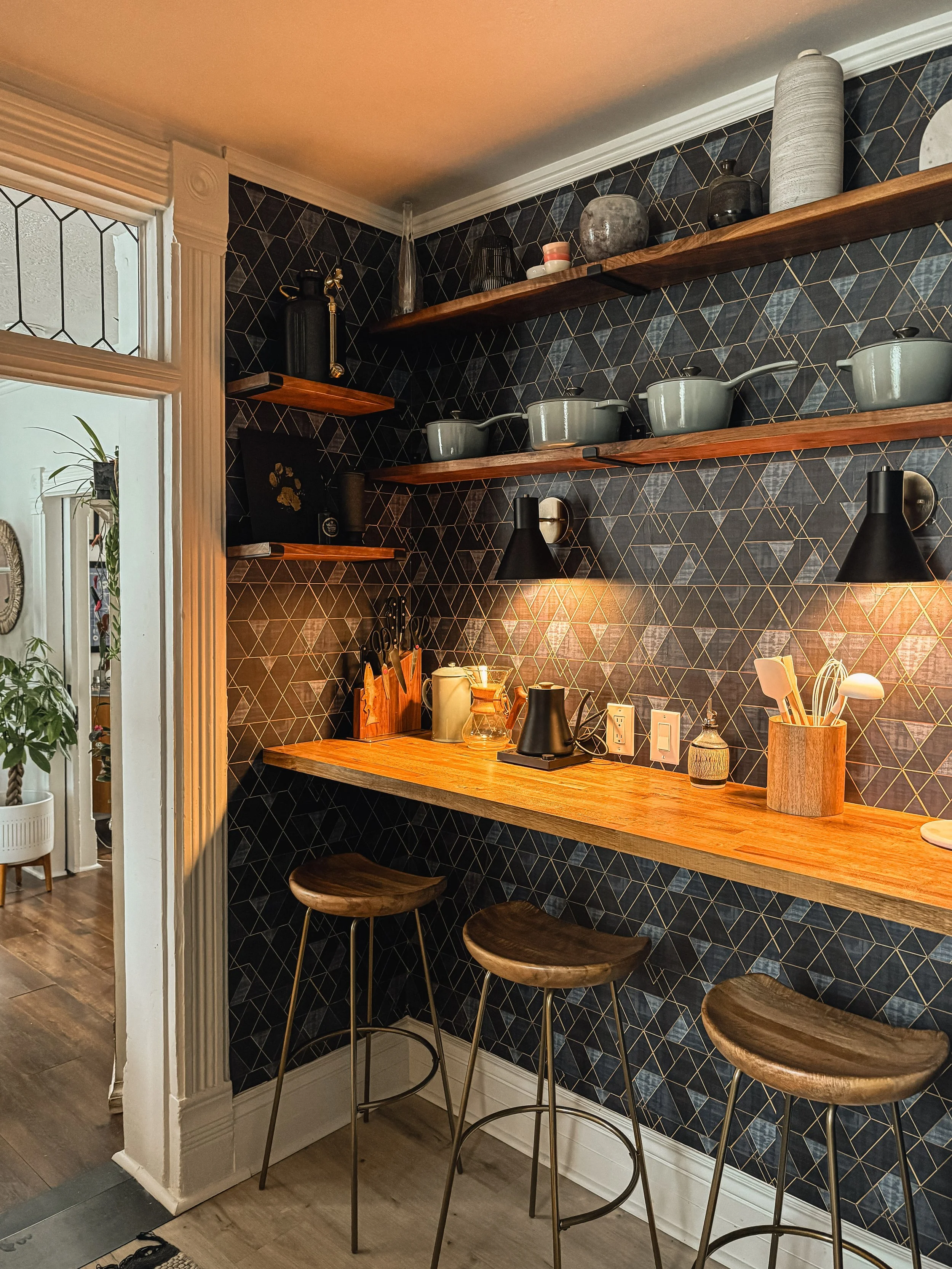 Dark tiled bar at the West Temple residence with open wood shelving, stools, ceramics, and warm accent lighting.