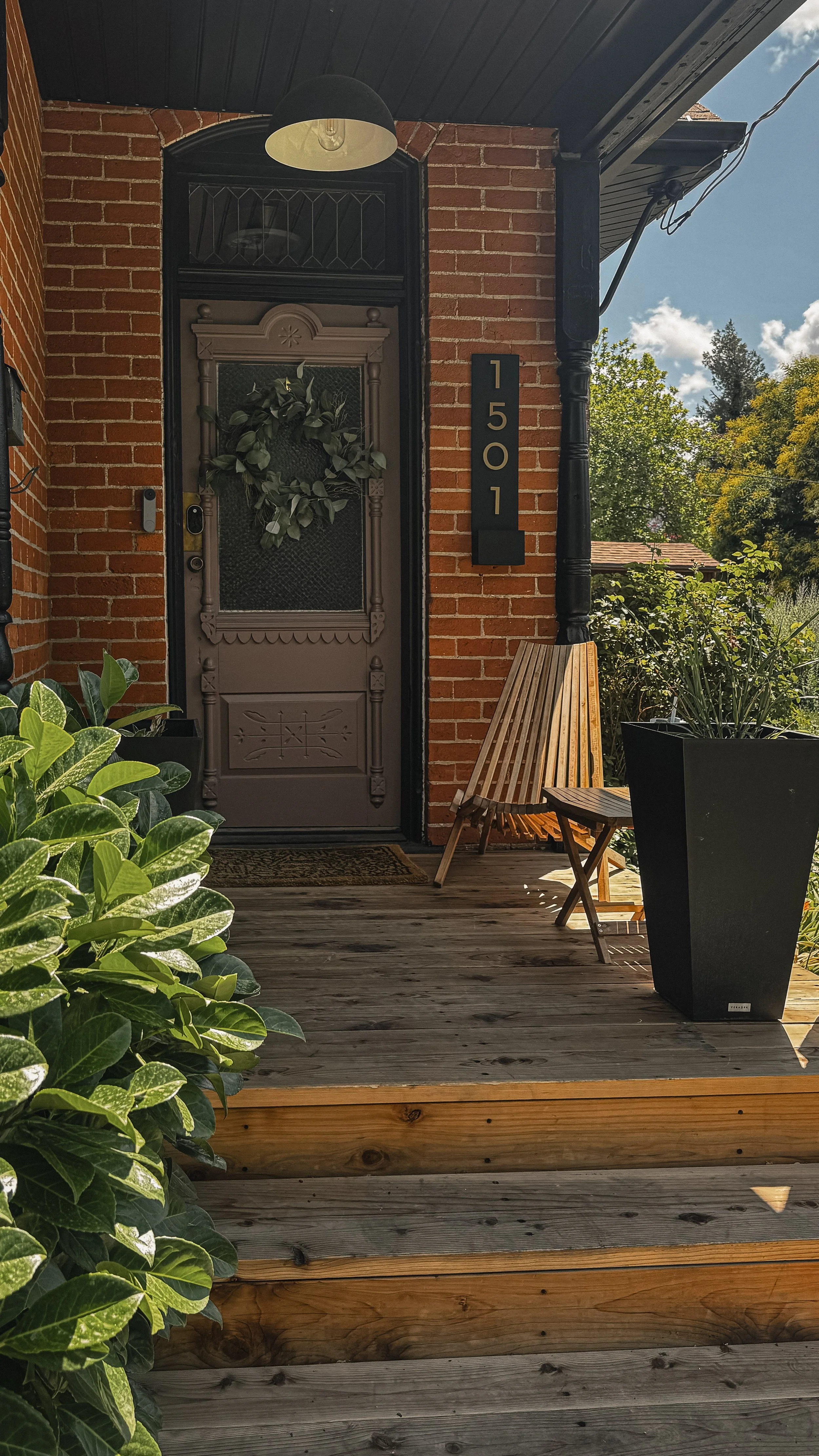Front entry of the West Temple residence in Salt Lake City with brick exterior, wood porch, dark front door, and surrounding greenery.