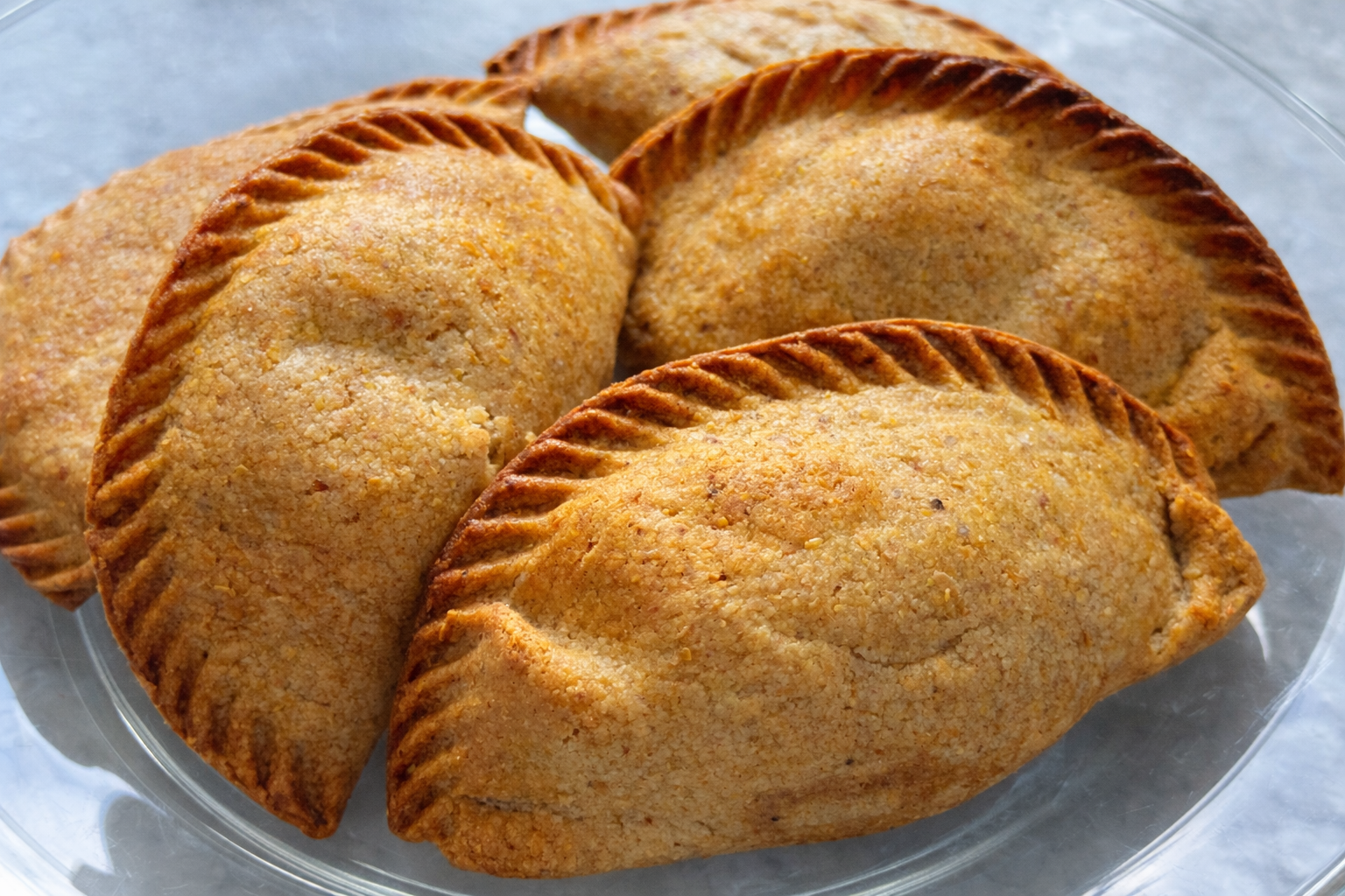 Four air fried high fiber empanadas on a clear glass plate, with golden-brown crust and crimped edges.
