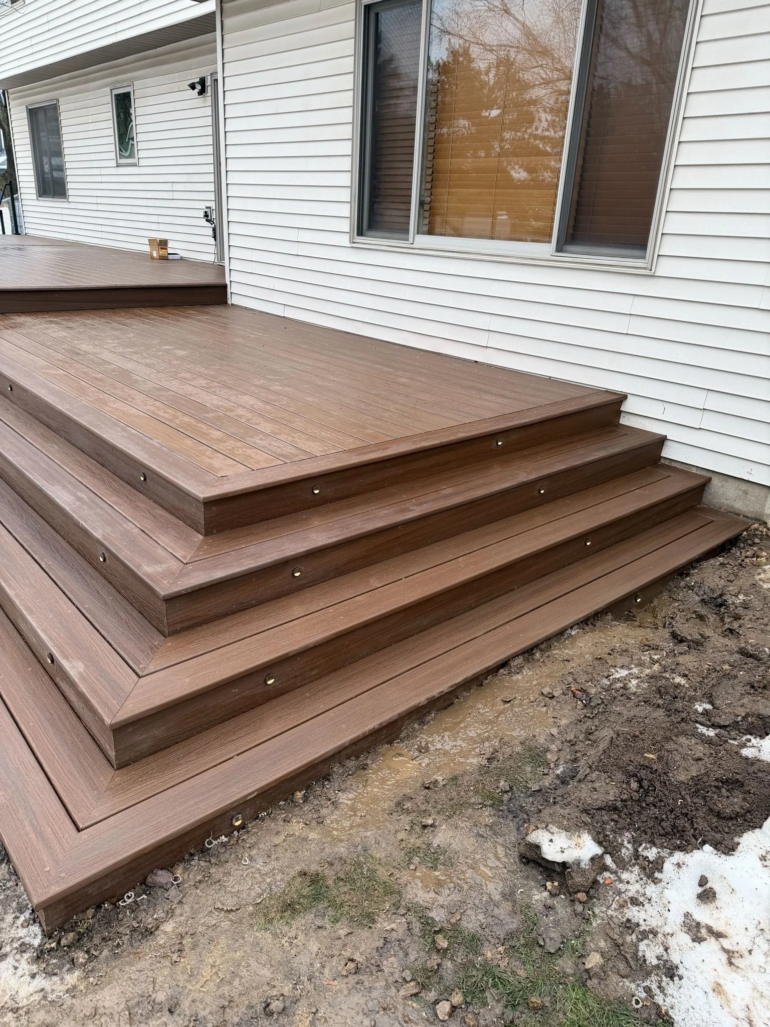 New wooden deck with stairs outside house with white siding and windows