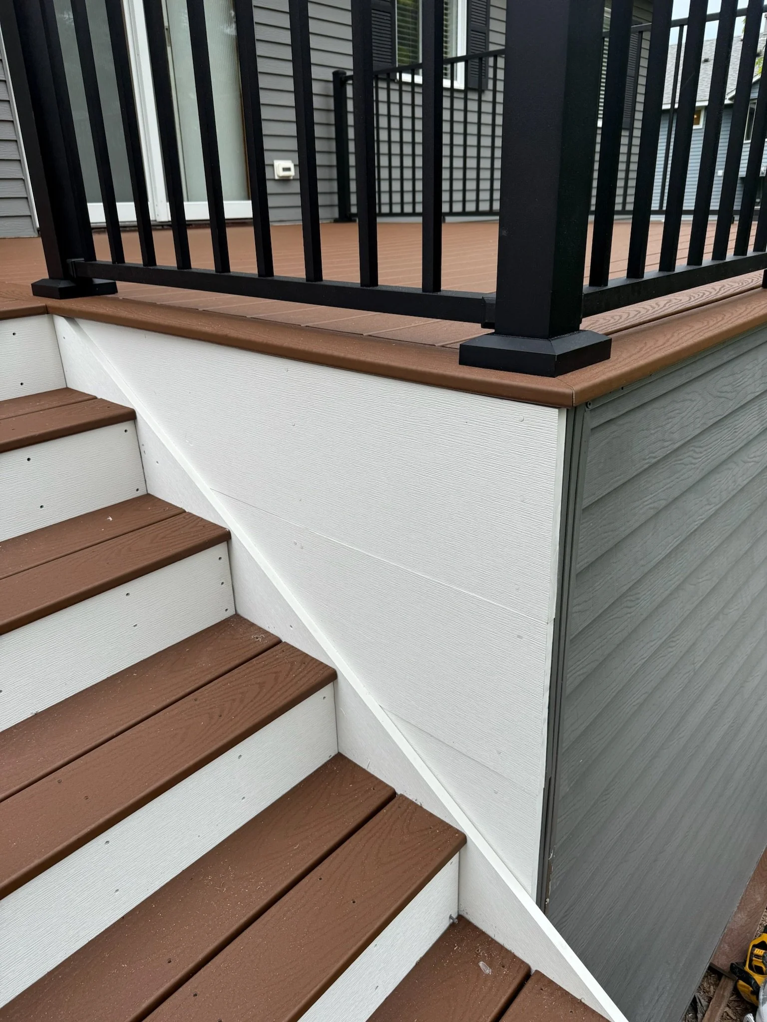 Close-up of stairs leading to a deck with brown wooden steps, white risers, and black metal railing on the deck.