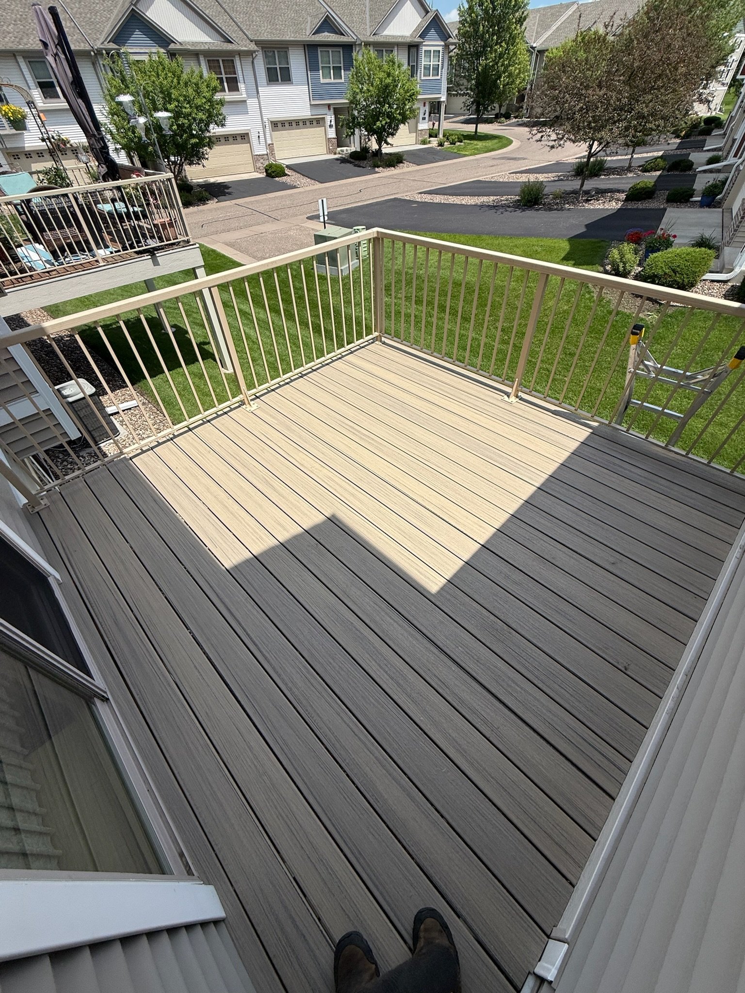 View from a balcony with new wooden decking and white railing, overlooking a residential neighborhood with well-maintained lawns, trees, and multi-story houses.