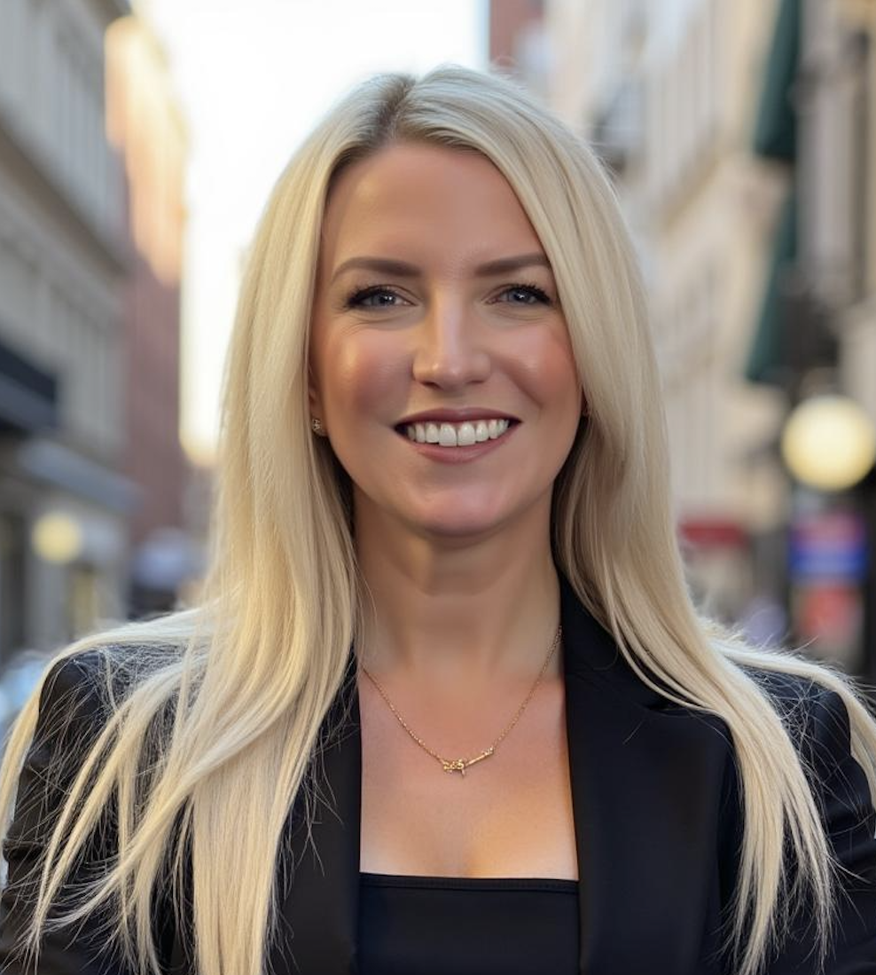 A portrait of a blonde woman smiling outdoors in an urban area.