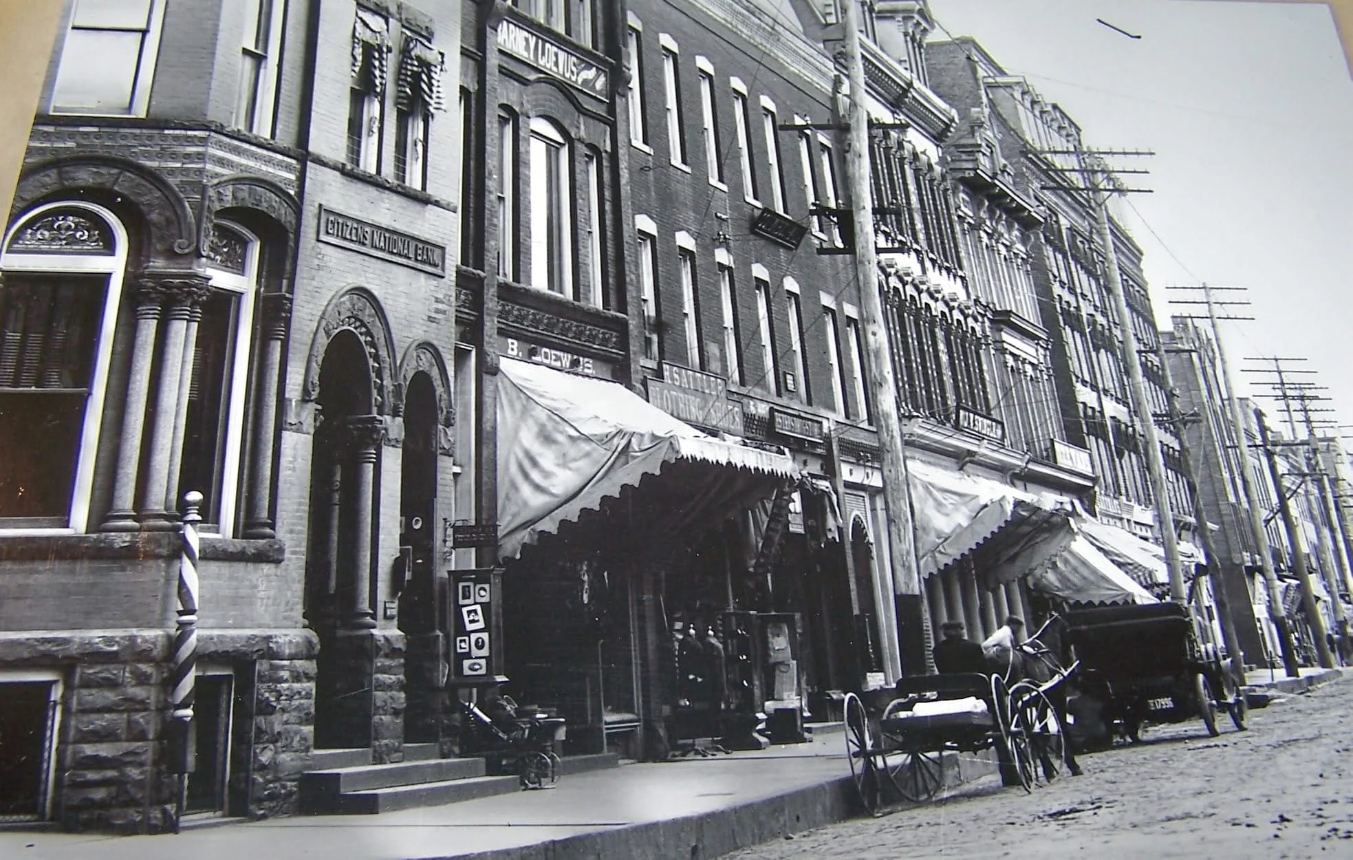 This close-up shot of the store fronts on Main Street shows the Citizens Bank at far-left. The first doorway went into the bank, while the smaller doorway next to it went upstairs to the Ott & Hay photography studio. Examples of photographs can be se