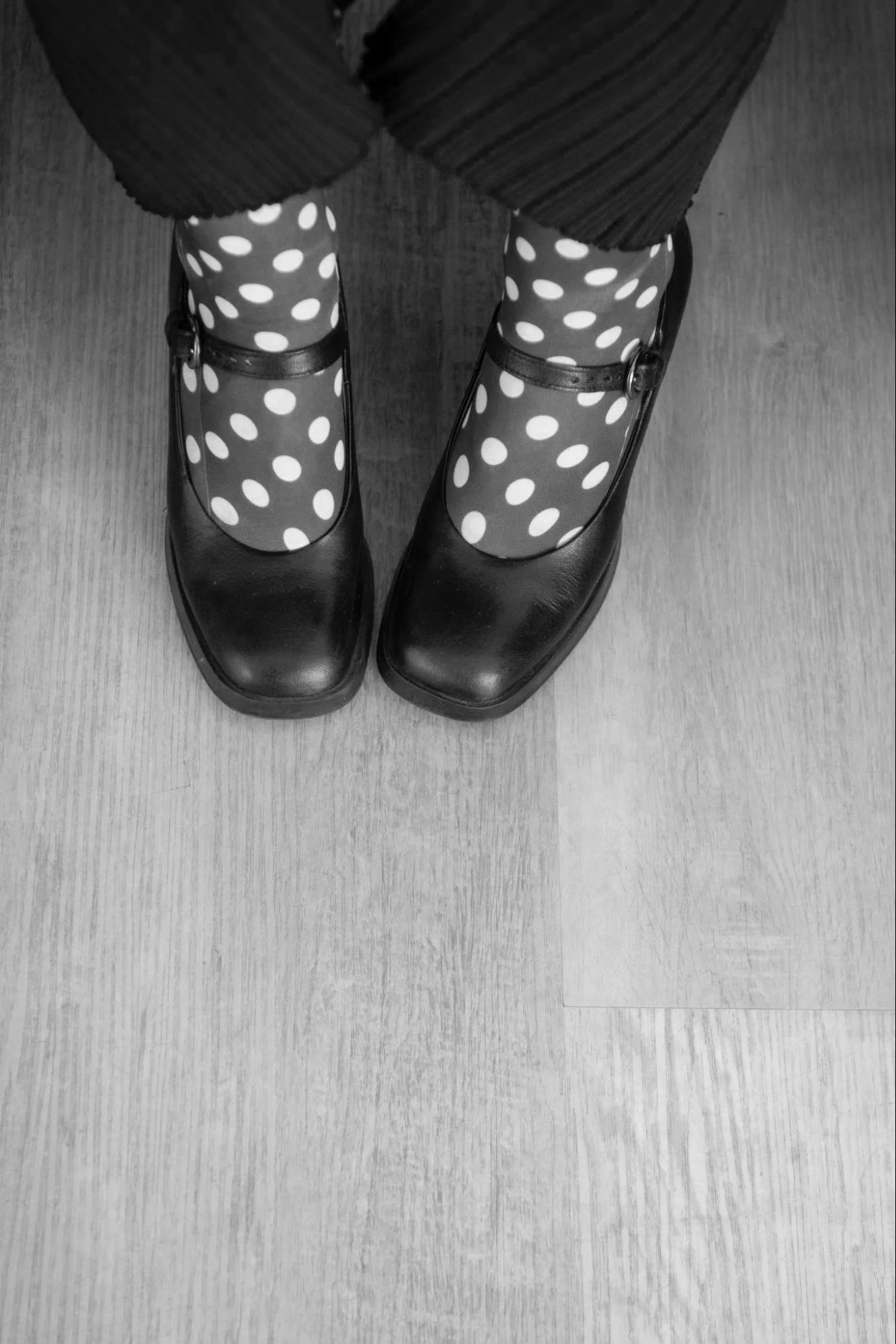 Black shoes worn with polka dot socks, viewed from above on a wooden floor.