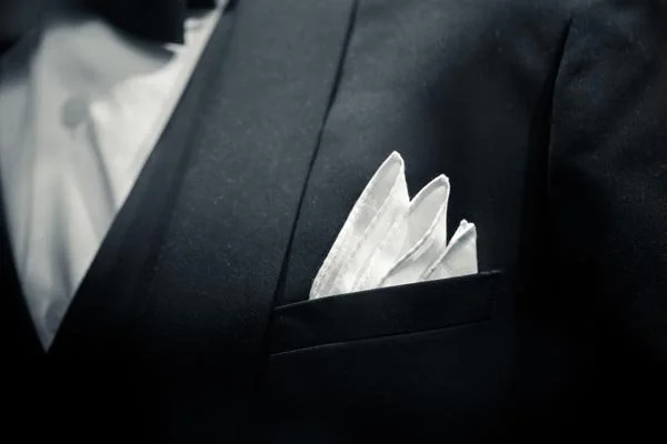 Close-up of a black suit jacket with a white pocket square in the breast pocket.