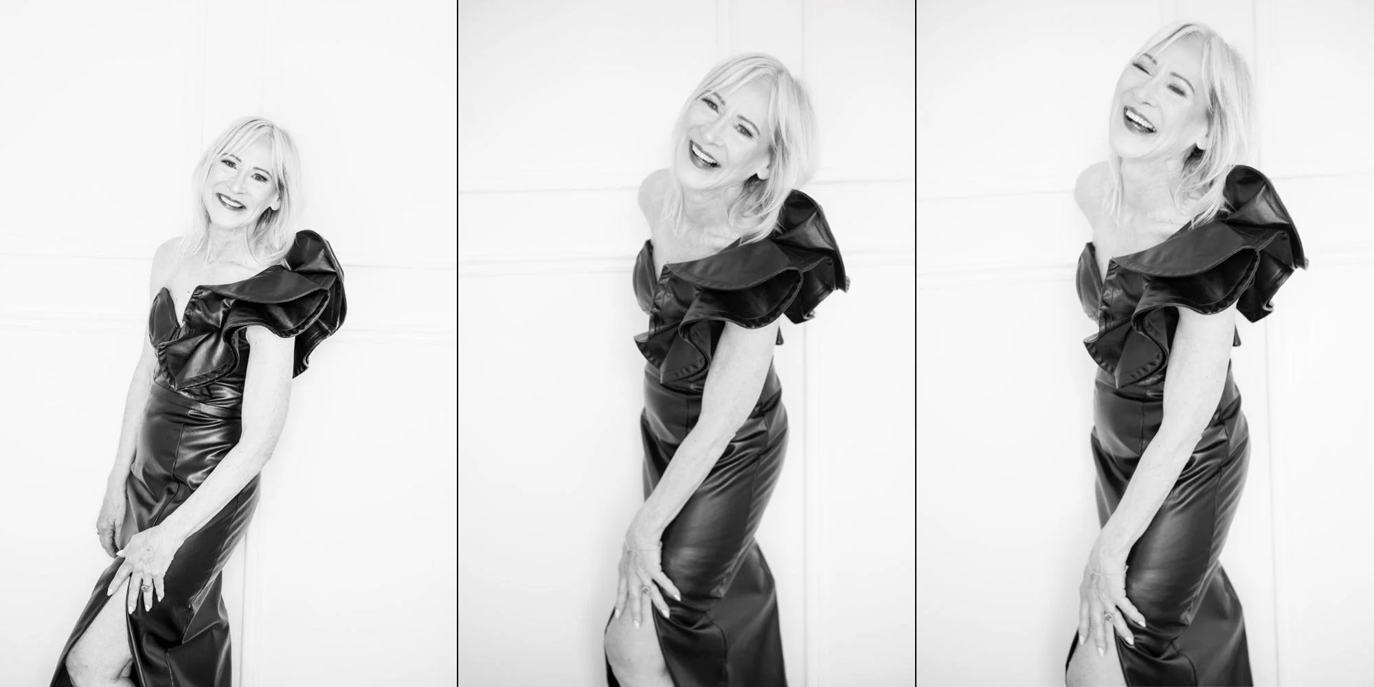 Black and white photo of a woman in a formal gown with ruffled shoulders, smiling and posing in front of a plain white wall.