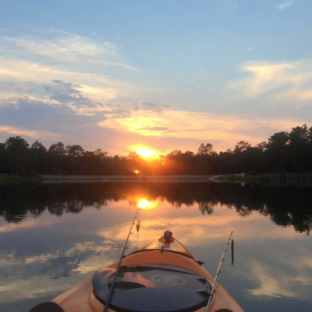 A kayak on a calm lake during sunset with trees on the shoreline and the sky reflected in the water.