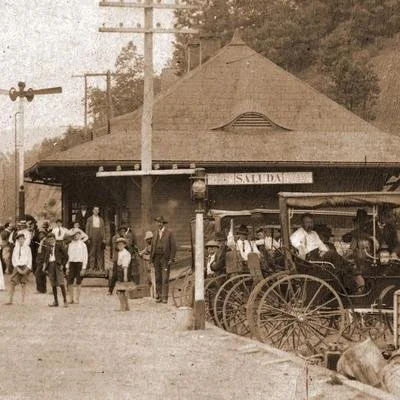 Vintage train station with people, a horse-drawn carriage in front, and a building with a sign that reads 'Salida'.