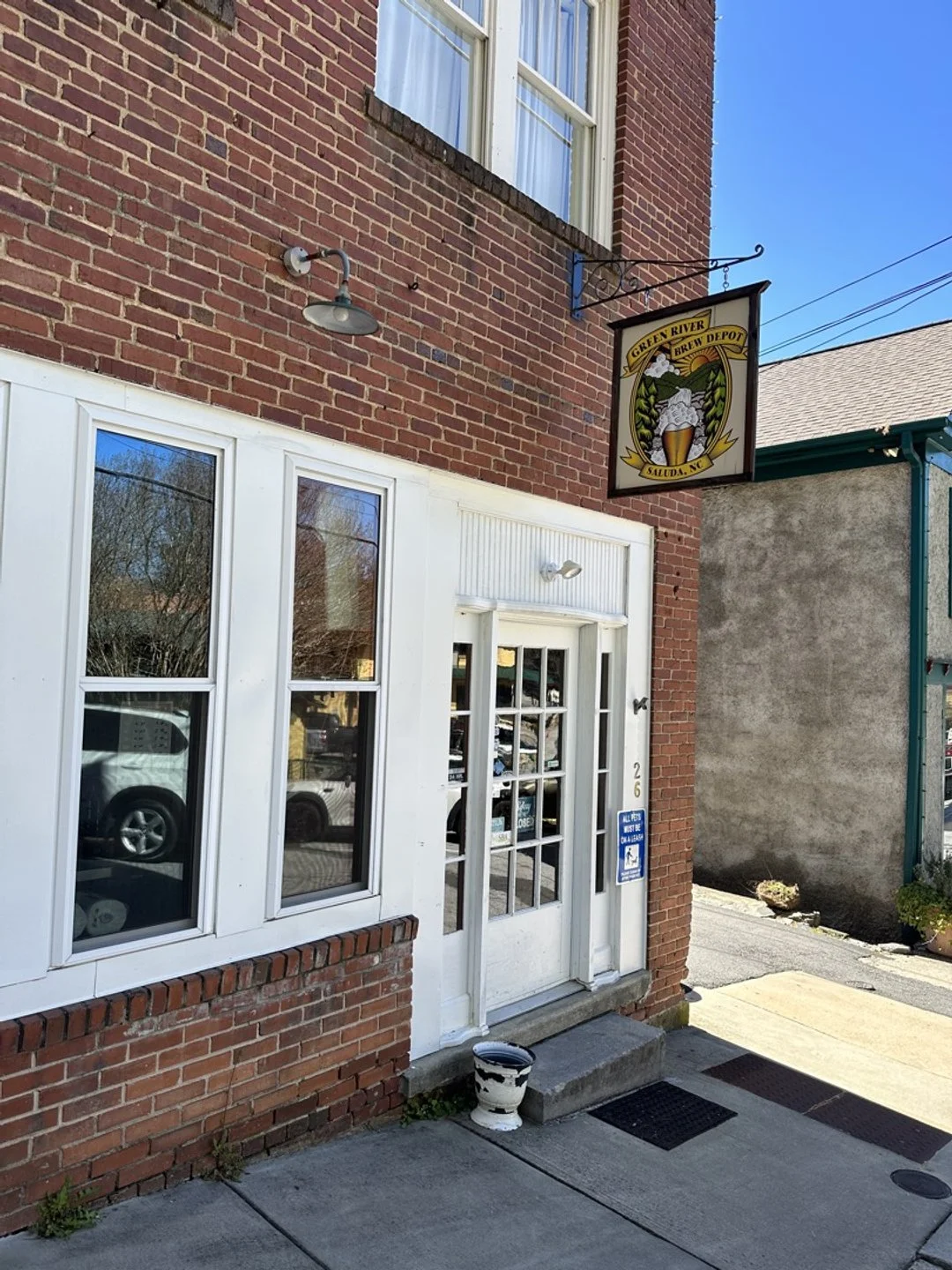 Exterior of a brick building with white window frames and a white door. A sign for Green River Brew Depot hangs above the entrance, showing a beer mug with steam and a scenic background. Small potted plant near the door.