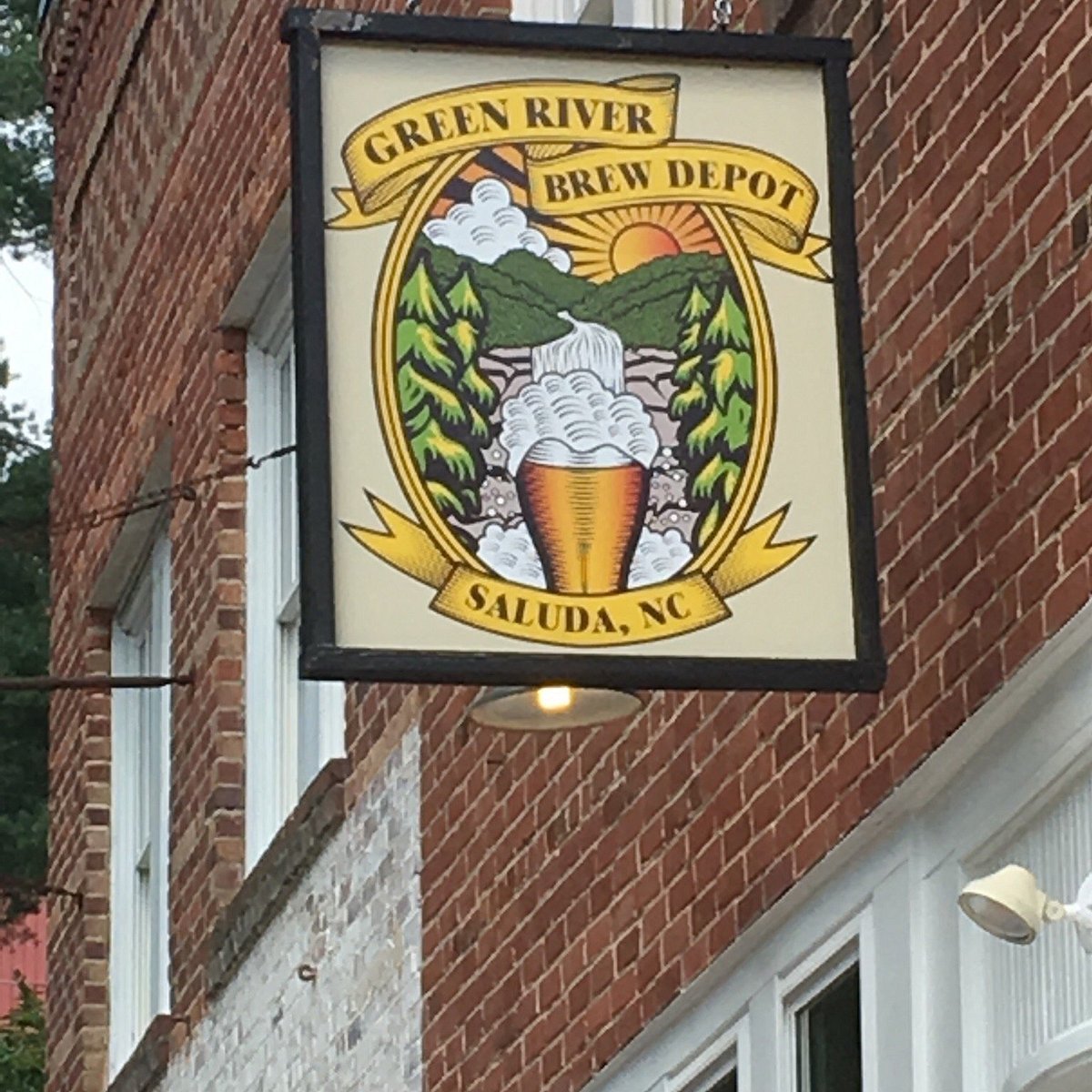 Sign for Green River Brew Depot in Saluda, North Carolina showing a mountain scene with a waterfall and a beer glass with foam, a setting sun, and trees.