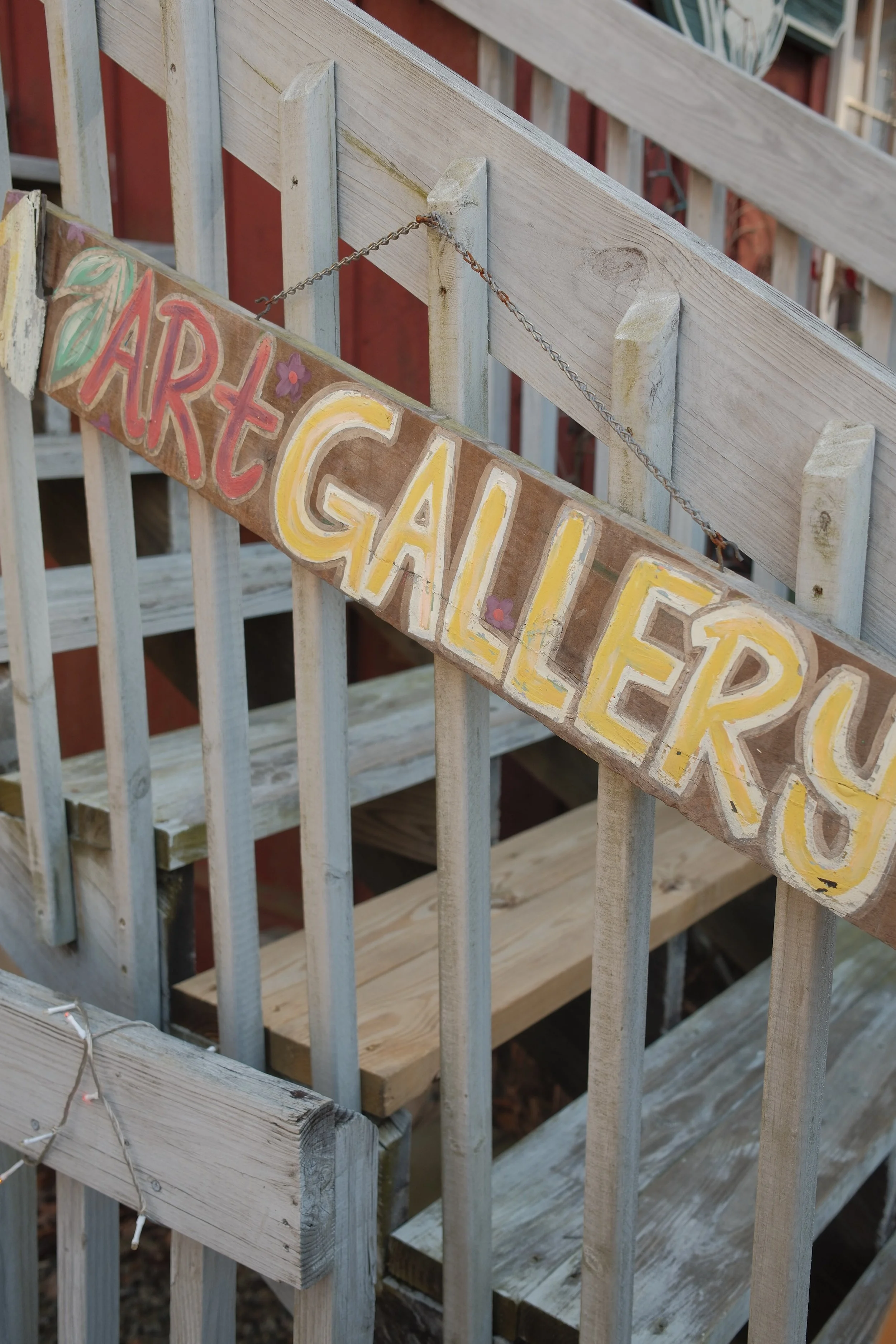 Wooden deck railing with painted and decorated sign saying "Fairy Garden" hanging from chain.