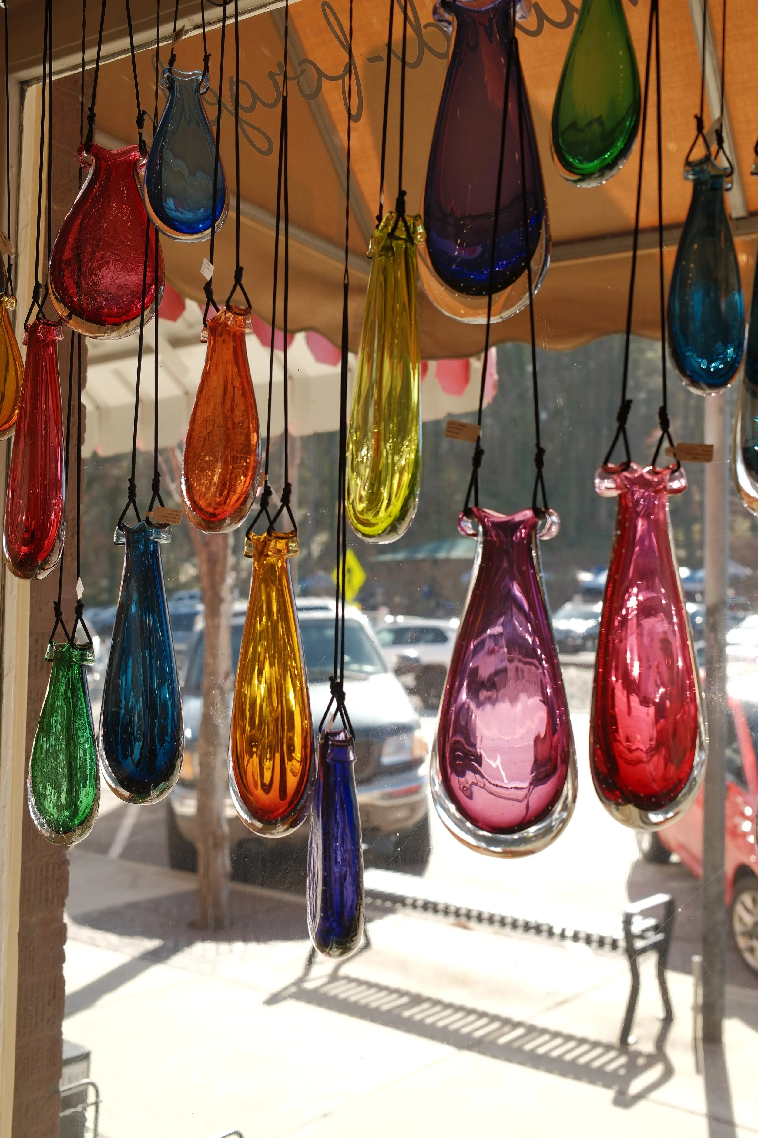 Colorful glass ornaments hanging in front of a window with sunlight streaming through, casting shadows outside.
