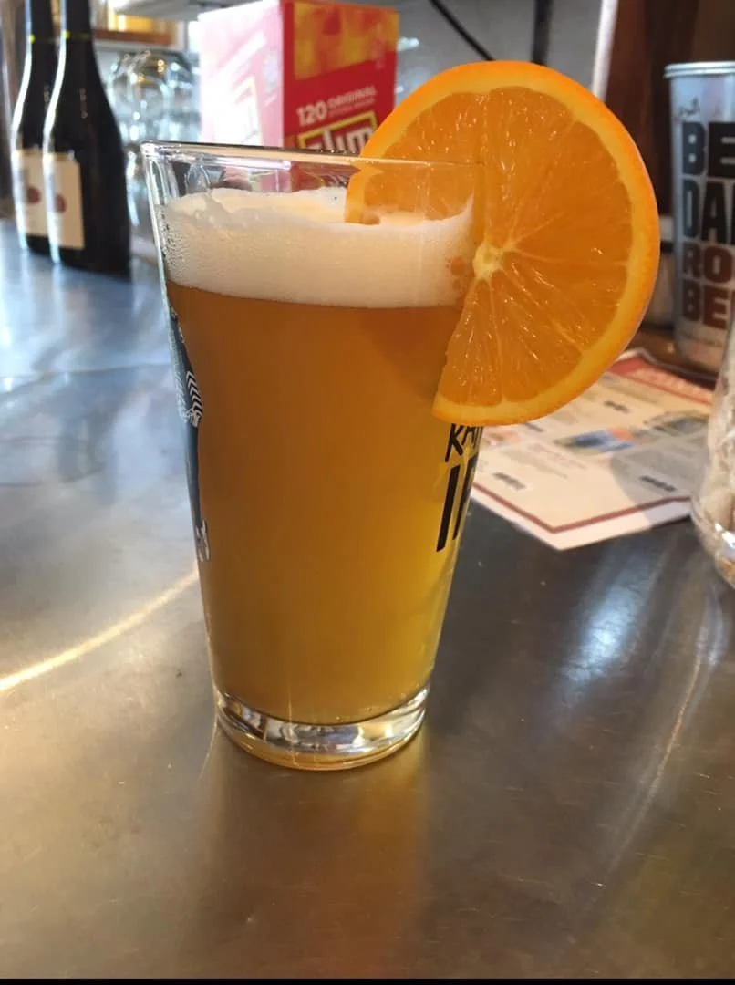A pint glass filled with beer and garnished with an orange slice on the rim, placed on a bar counter.