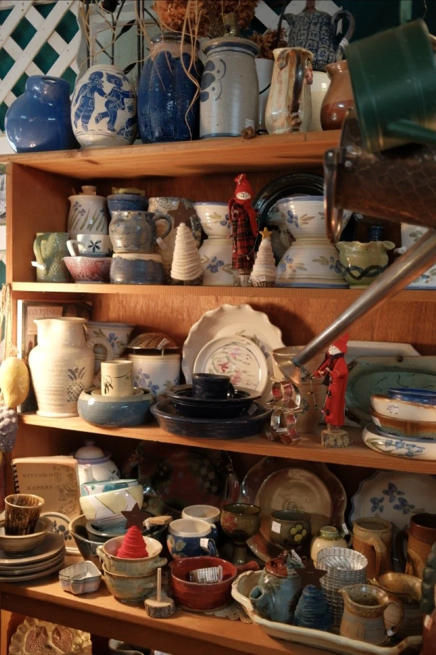 Wooden shelves filled with various pottery and ceramic dishware, including cups, bowls, and vases, along with decorative items like small reindeer figures and a Santa Claus ornament.
