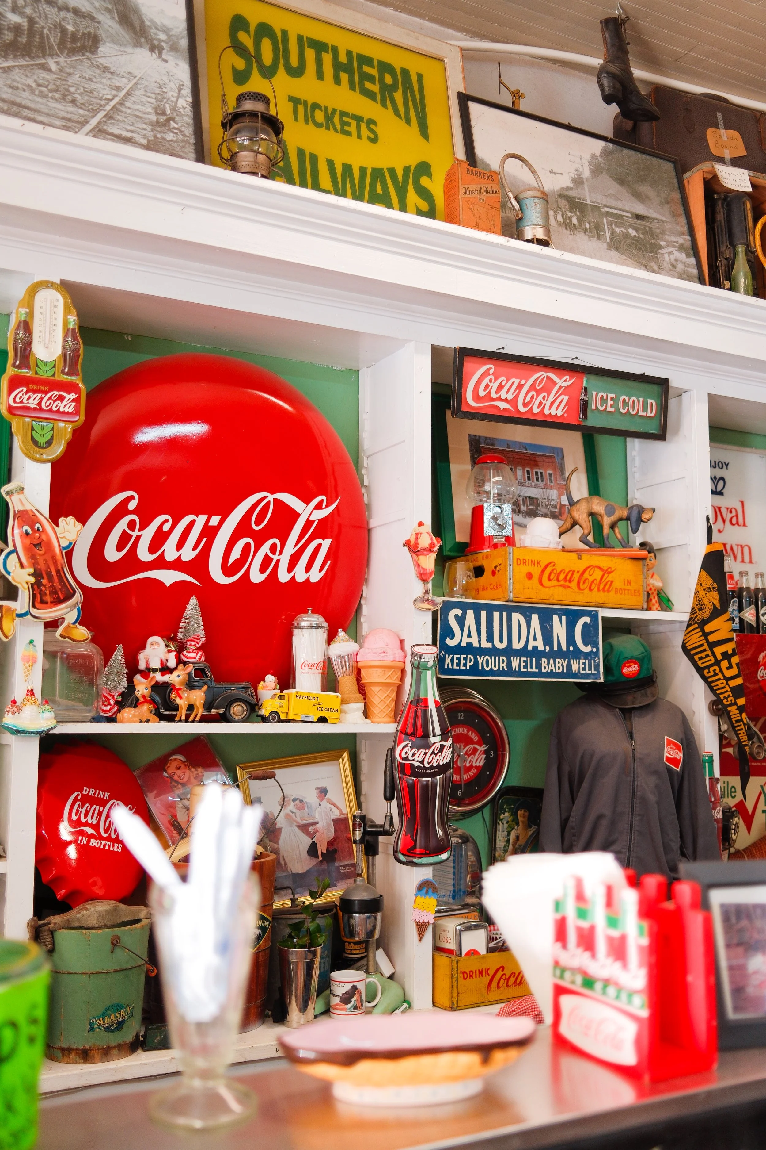 Decorative vintage items including Coca-Cola signs, small figurines, and memorabilia on shelves in a nostalgic shop or cafe.