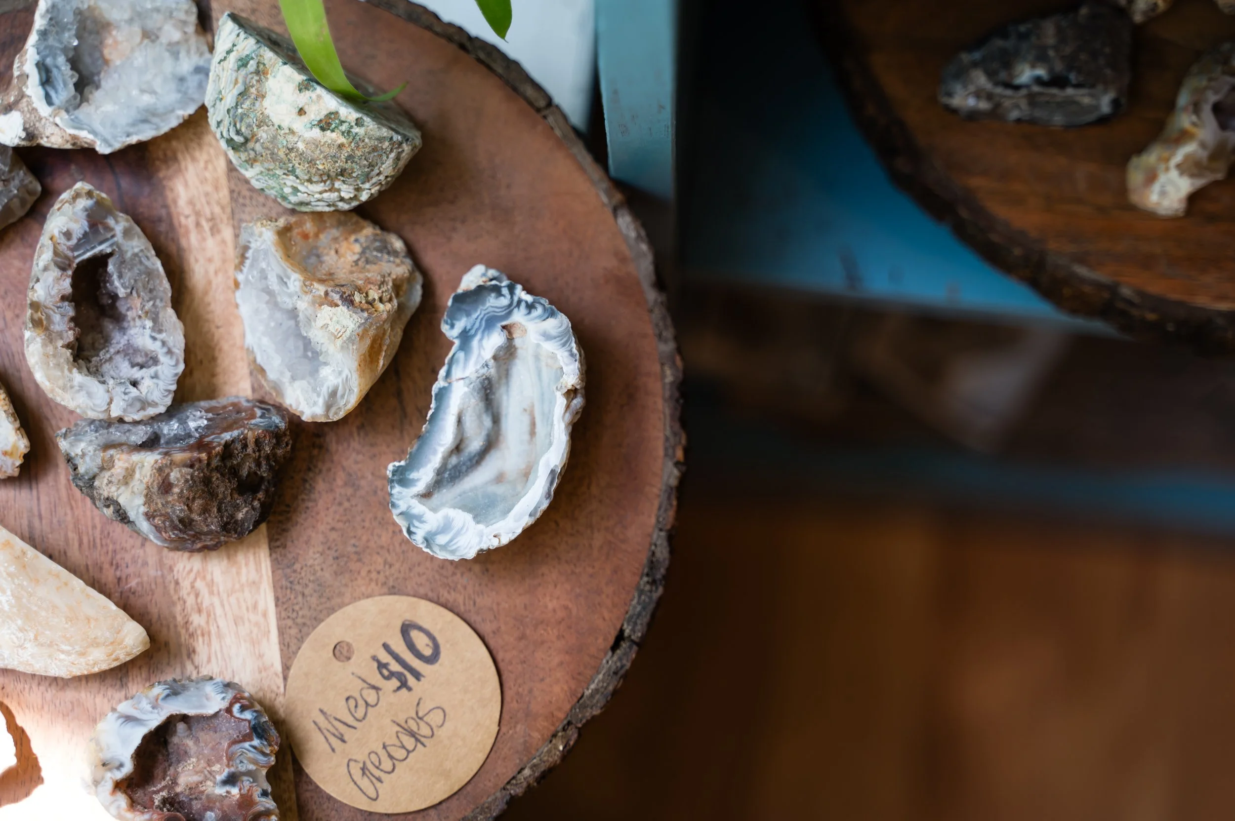 Close-up of various geode and agate rocks displayed on a wooden surface, with a handwritten price tag reading '$10' visible.