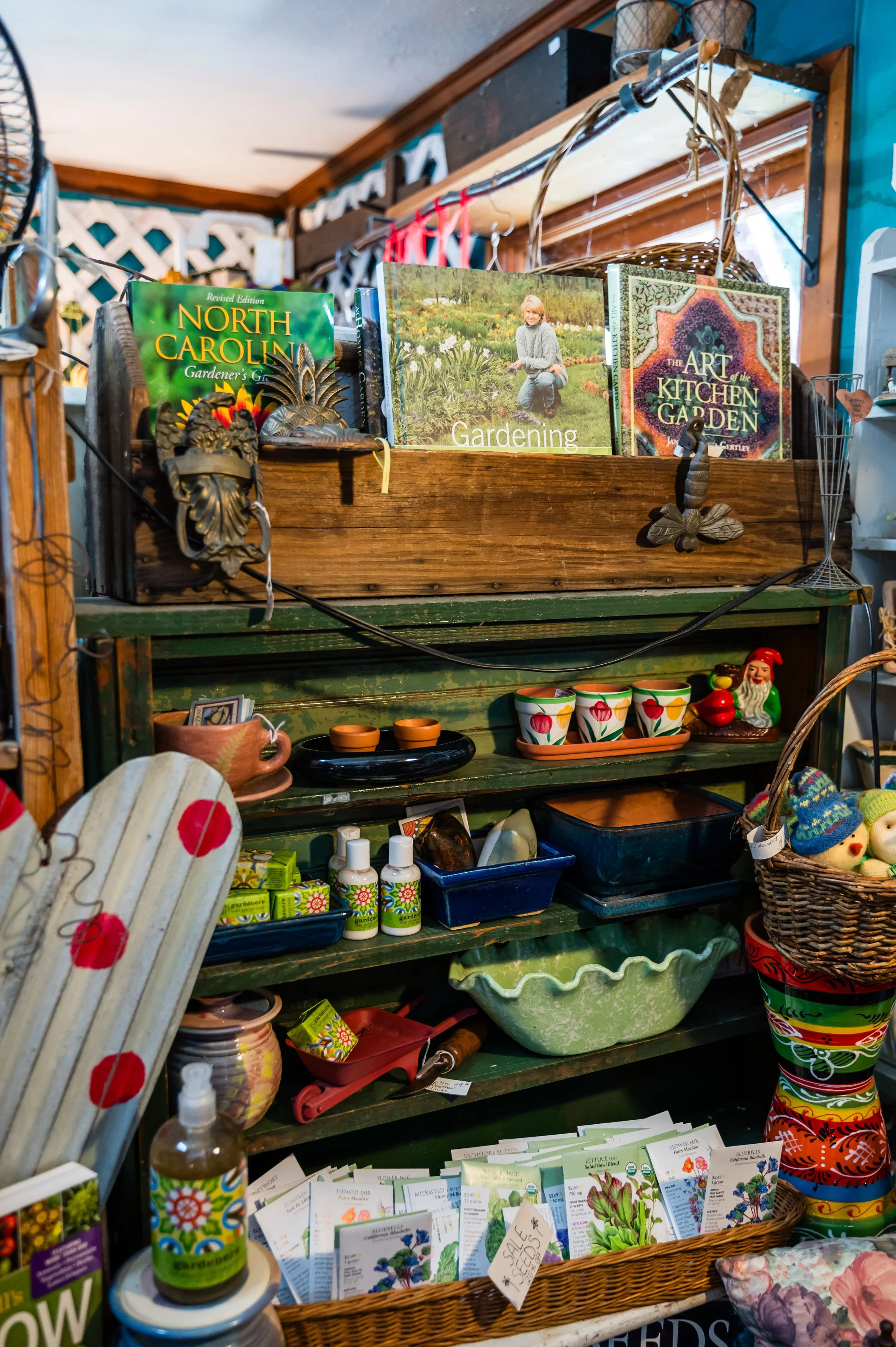Shelves filled with gardening books, seed packets, small pots, decorative items, and gardening supplies in a store.
