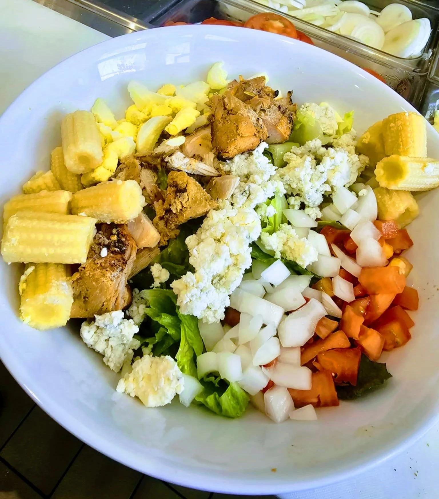 Bowl of fresh chopped vegetables and cheese, including cauliflower, cherry tomatoes, onions, green peppers, and crumbled feta cheese, placed on a table.