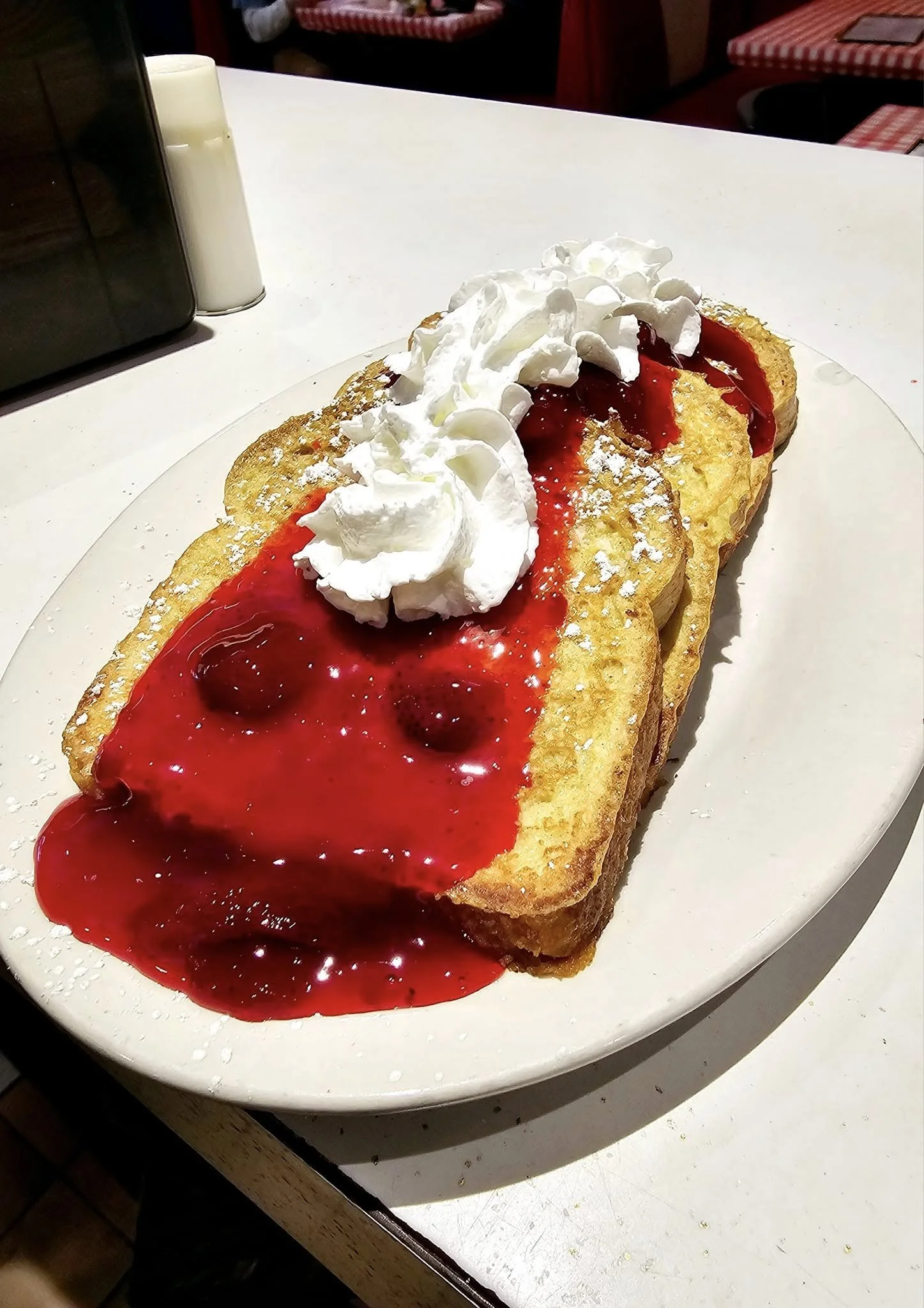 French toast topped with whipped cream and berry sauce on a white plate.