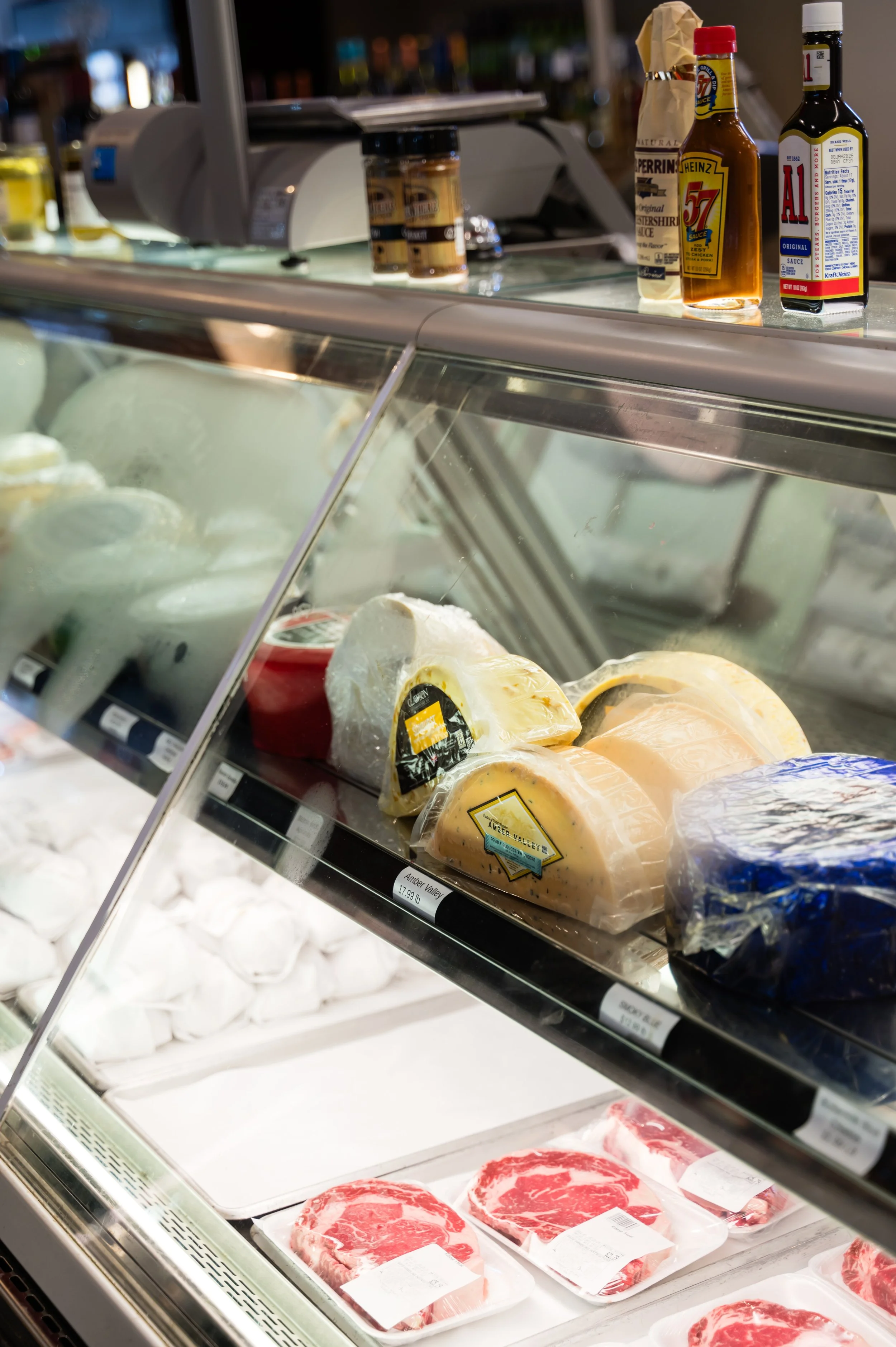 Glass refrigerated display case with cuts of raw red meat, including steaks and roasts, on white styrofoam trays in a grocery store or butcher shop.