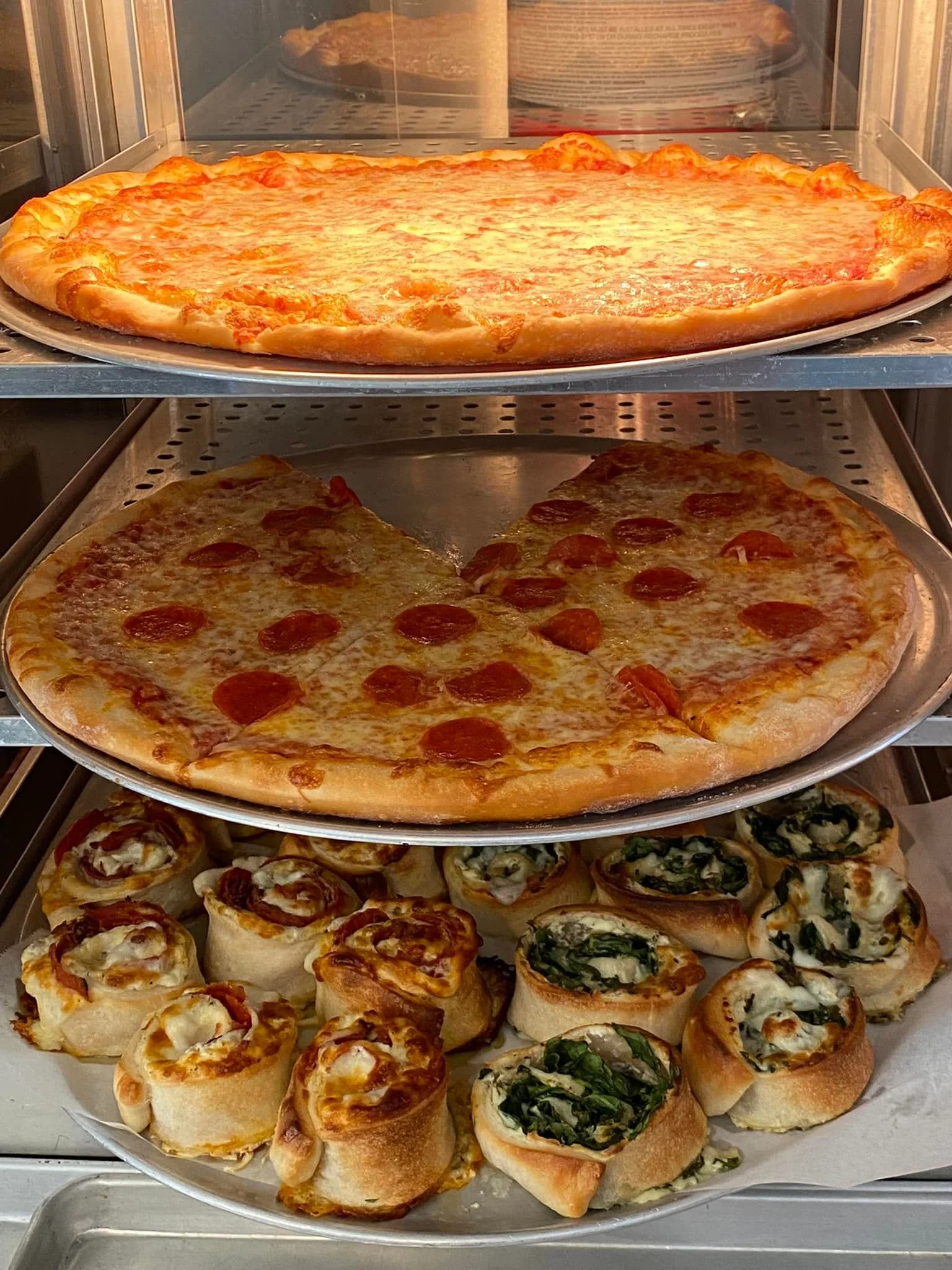 Three shelves of assorted pizzas, including cheese, pepperoni, and vegetable toppings.