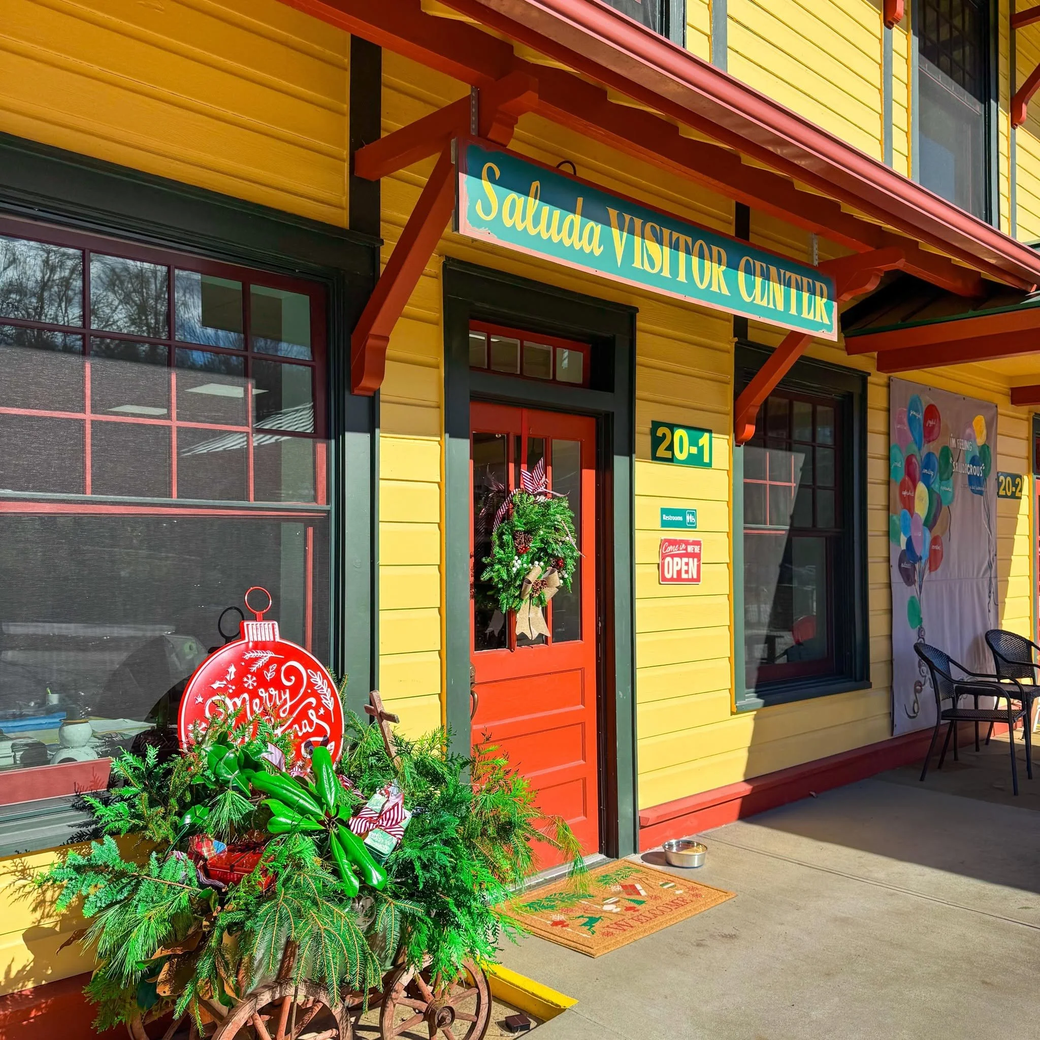 Colorful exterior of a visitor center with a yellow wooden wall, orange trim, and large windows. There are holiday decorations, including a wreath and a sign that reads 'Merry Christmas.'