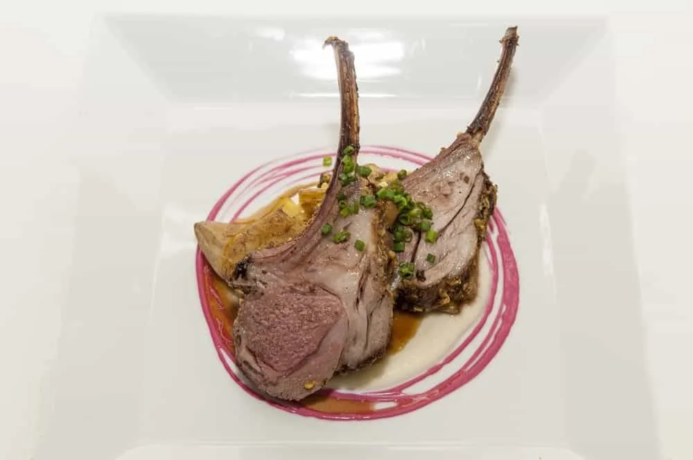 Two cooked lamb loin chops garnished with chopped green herbs, served on a decorative plate with sauce.
