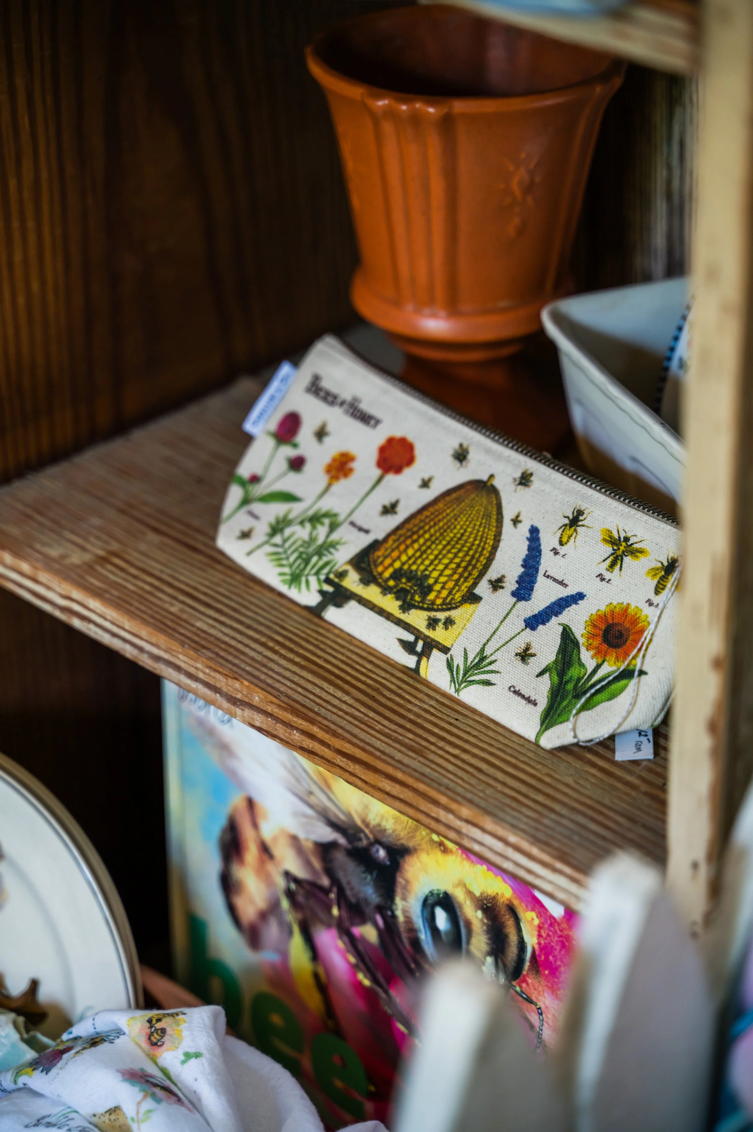A small, illustrated botanical print featuring various flowers and bees, positioned on a wooden shelf among other decorative items.