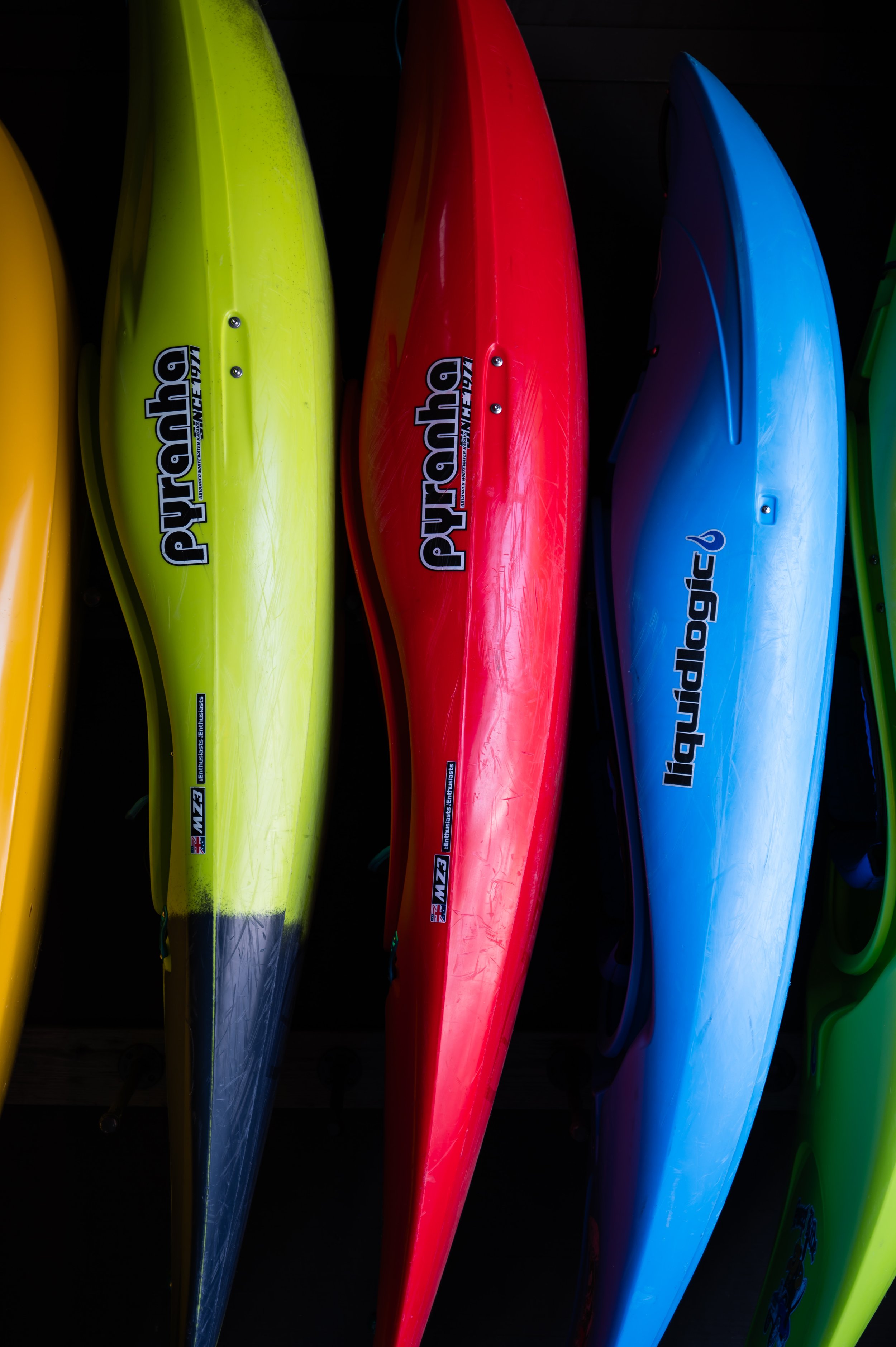 Colorful kayaks lined up vertically in yellow, green, red, blue, and green colors.