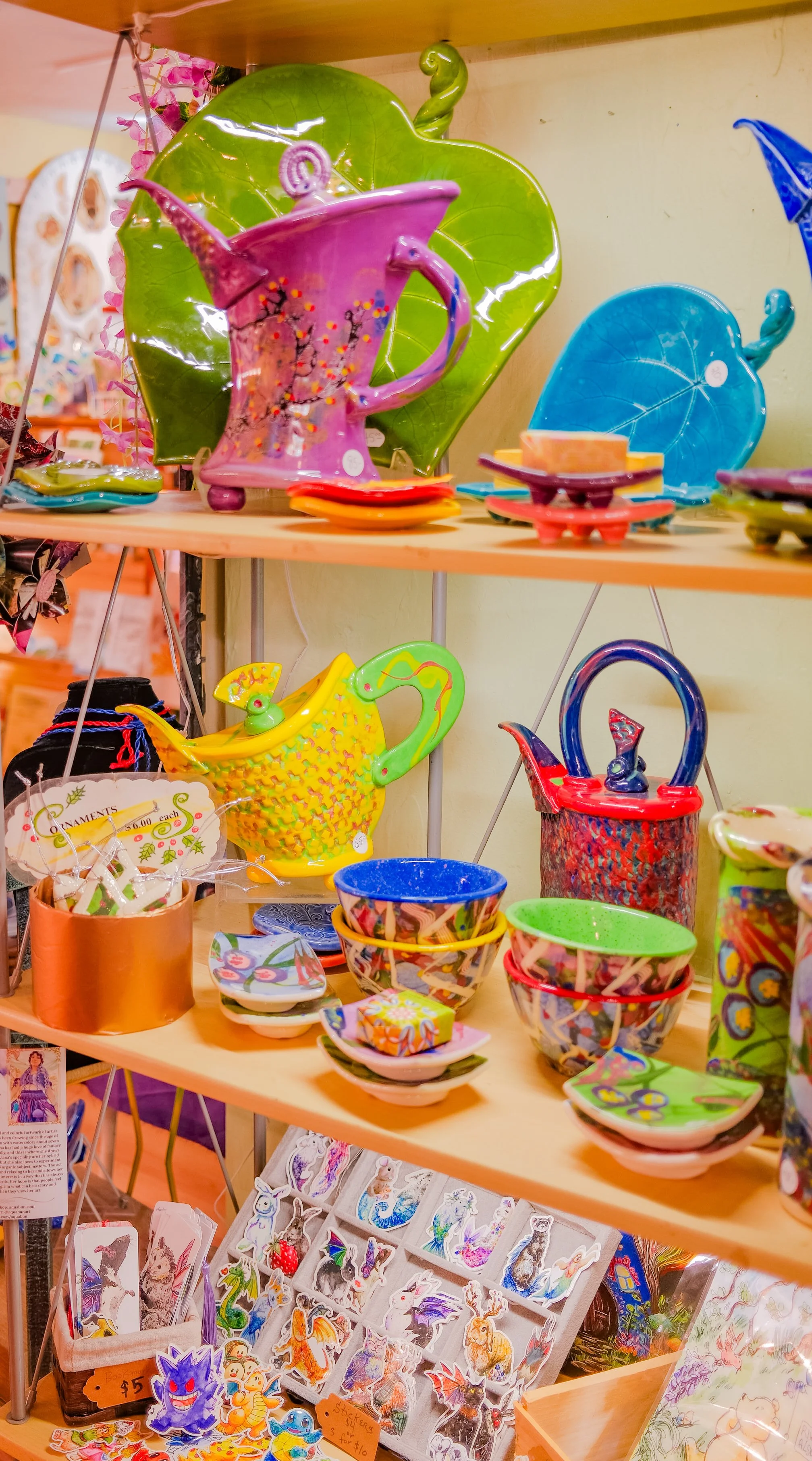 Colorful ceramic and glass items including teapots, cups, and decorative pieces arranged on shelves at a shop.