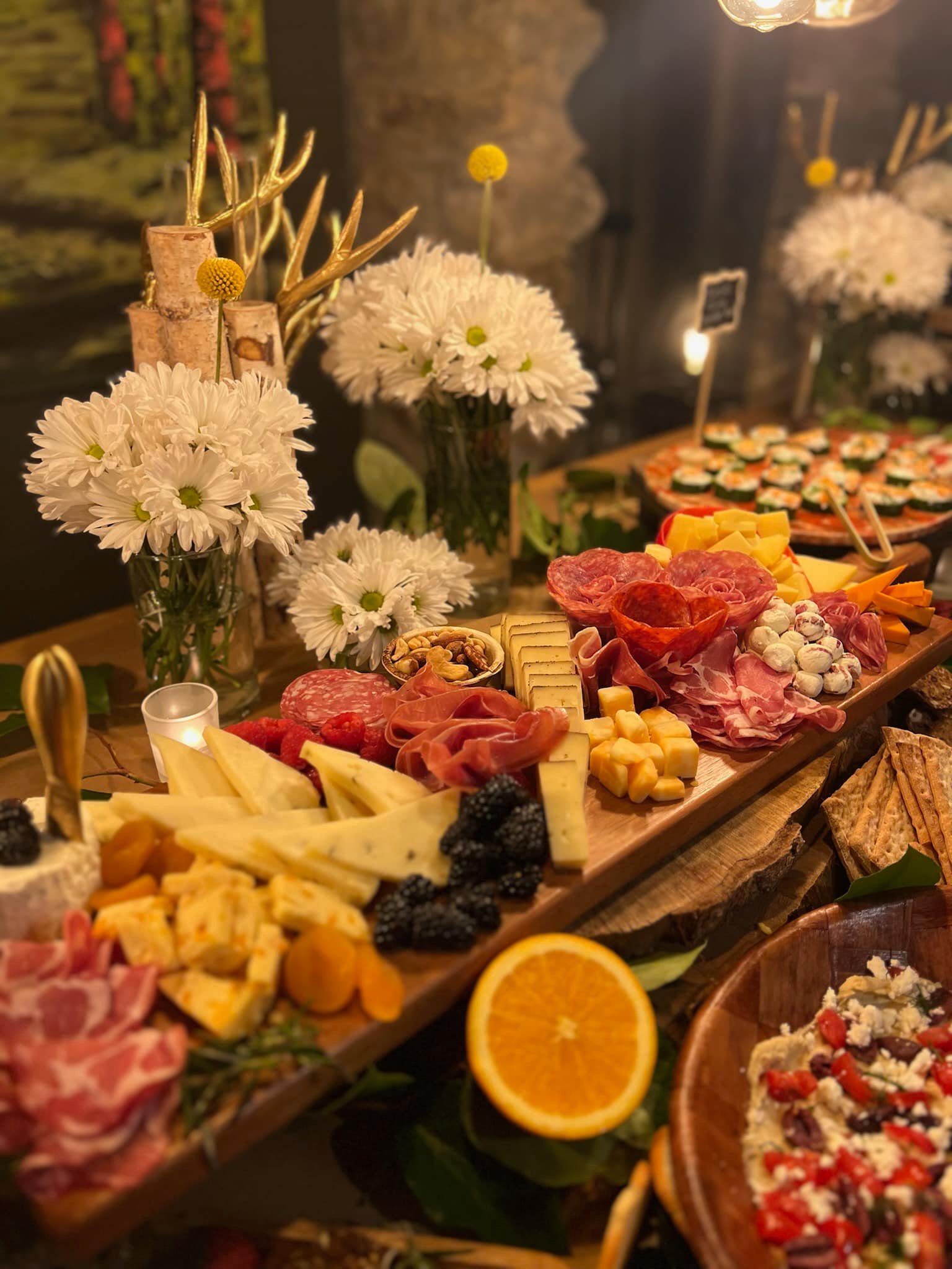 A cheese and charcuterie board with assorted cheeses, cured meats, fruits, nuts, and crackers, decorated with sliced oranges and white flowers.