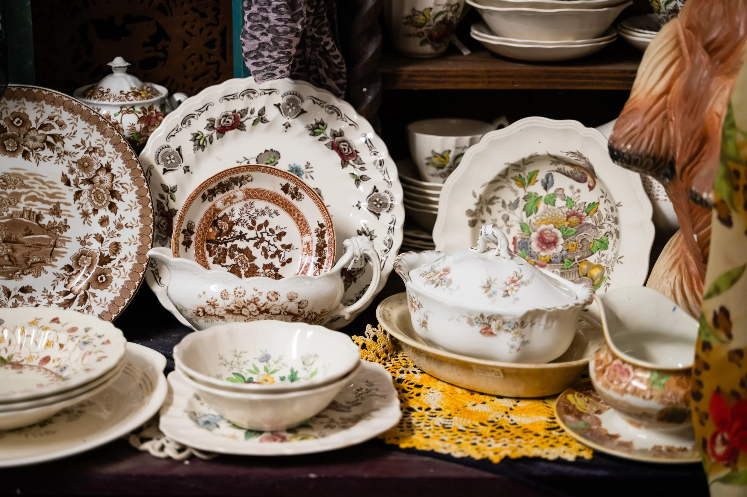 Collection of vintage decorative plates and bowls with floral and landscape patterns displayed on a shelf.