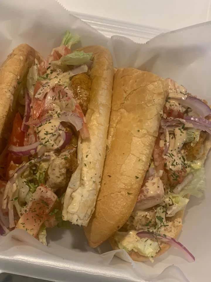 Two subs filled with salad, sliced tomatoes, red onions, and herbs, placed in a white takeout container.