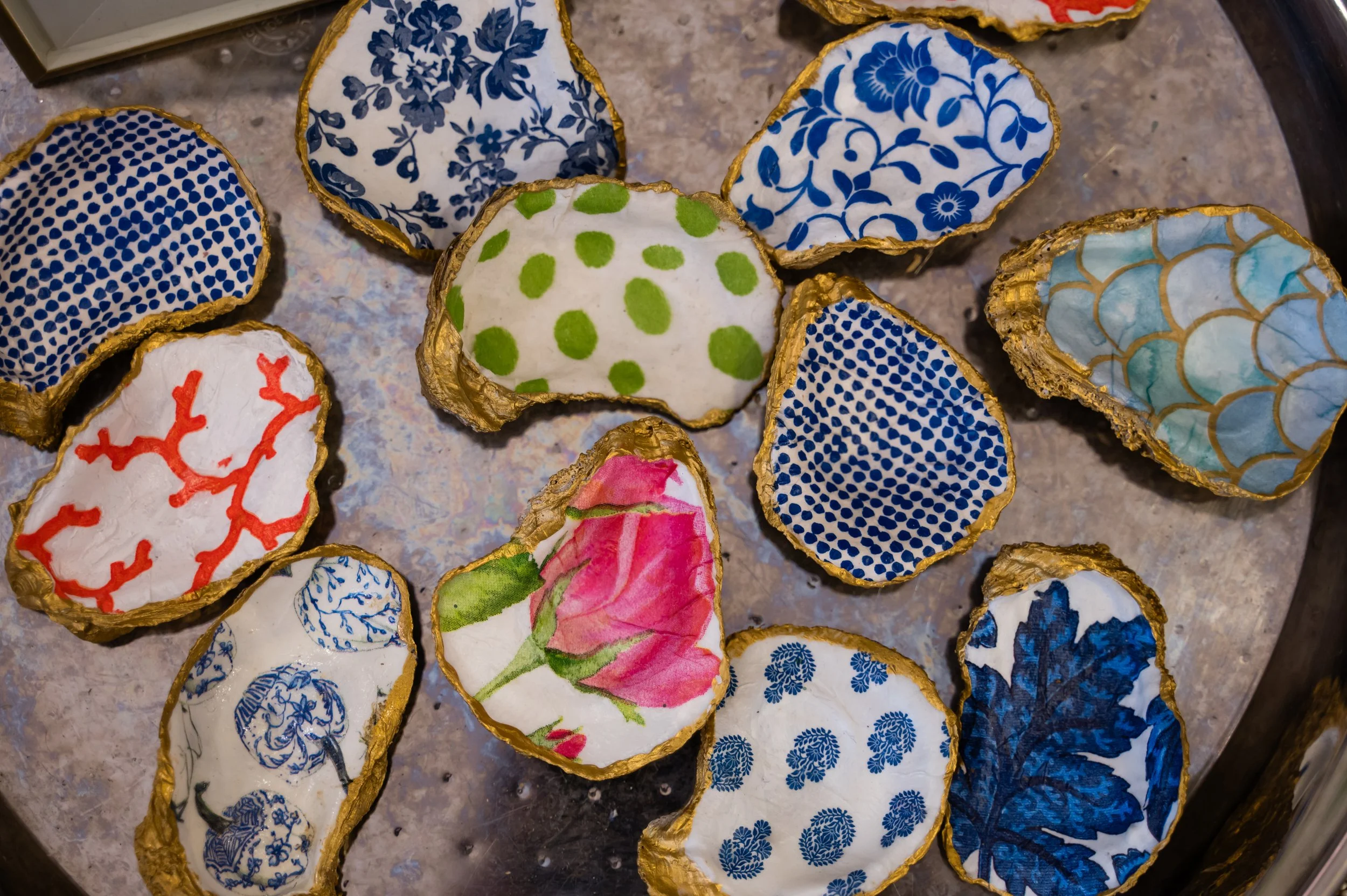 Decorative cutouts resembling stones or eggs, lined with gold, featuring various intricate blue, red, pink, and green patterns and floral designs on white backgrounds, arranged on a surface.