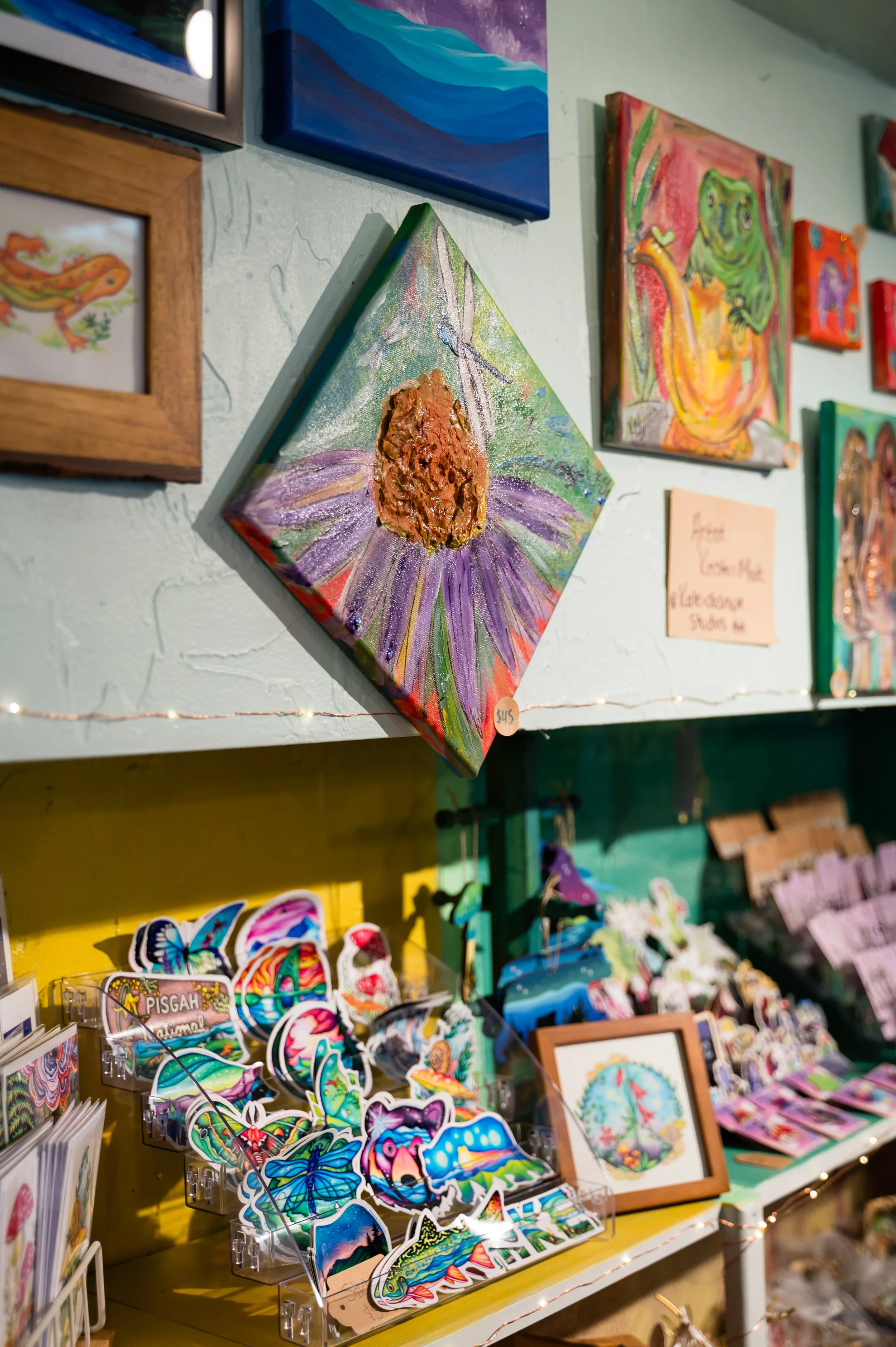 Wall decorated with colorful paintings of animals, landscapes, and abstract art, along with a display of butterfly and insect stickers, and various small items, including framed art and decorative objects.
