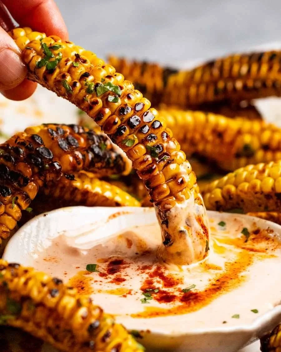 Grilled corn on the cob dipped in creamy spicy dipping sauce that is garnished with chopped herbs.