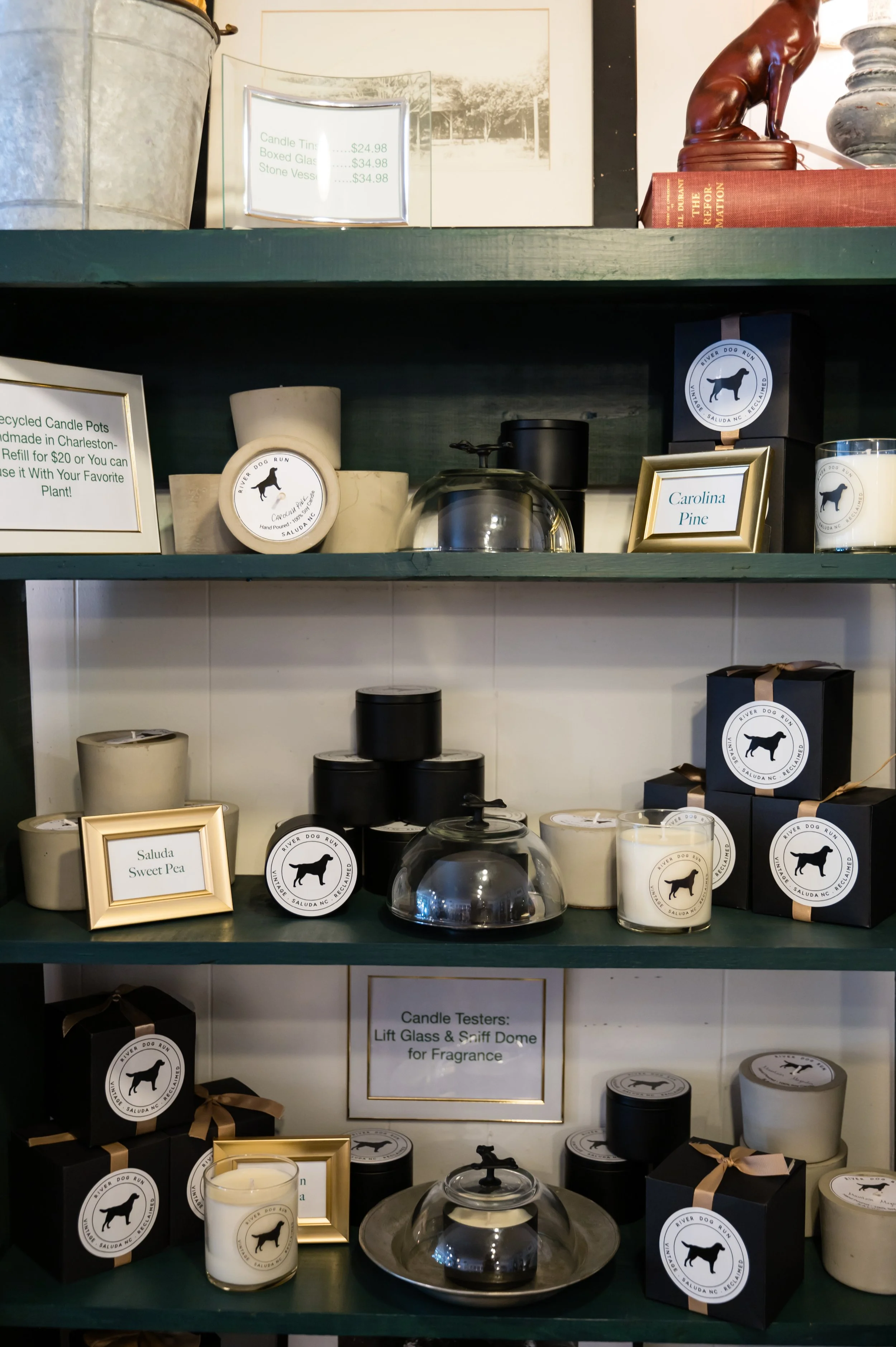Shelves displaying various candles, candle holders, and decorative items, including a framed sign about candle reuse and a glass dome with a candle inside.