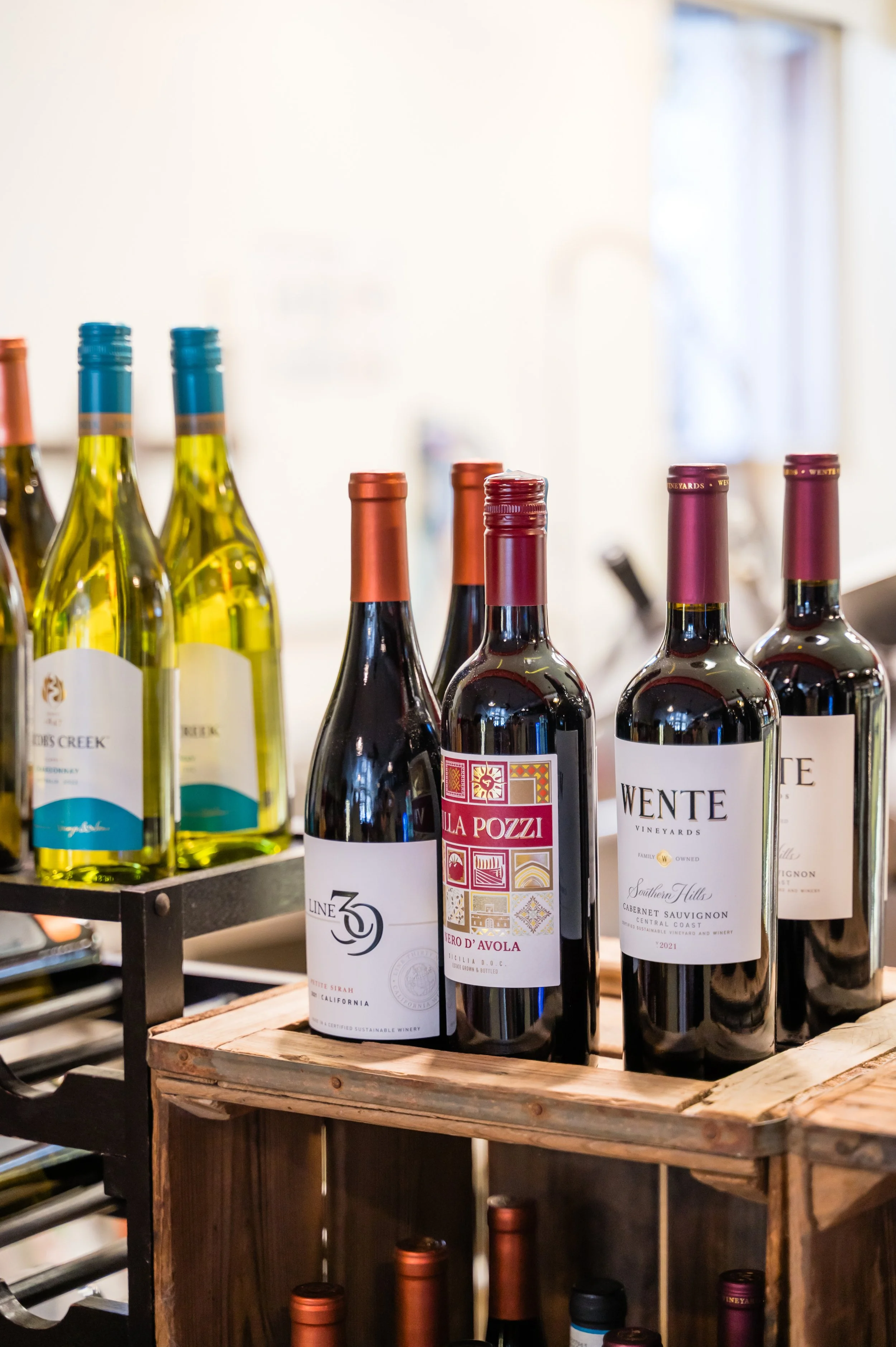 Various bottles of wine displayed on a wooden shelf, including red and white wine bottles with different labels and caps.