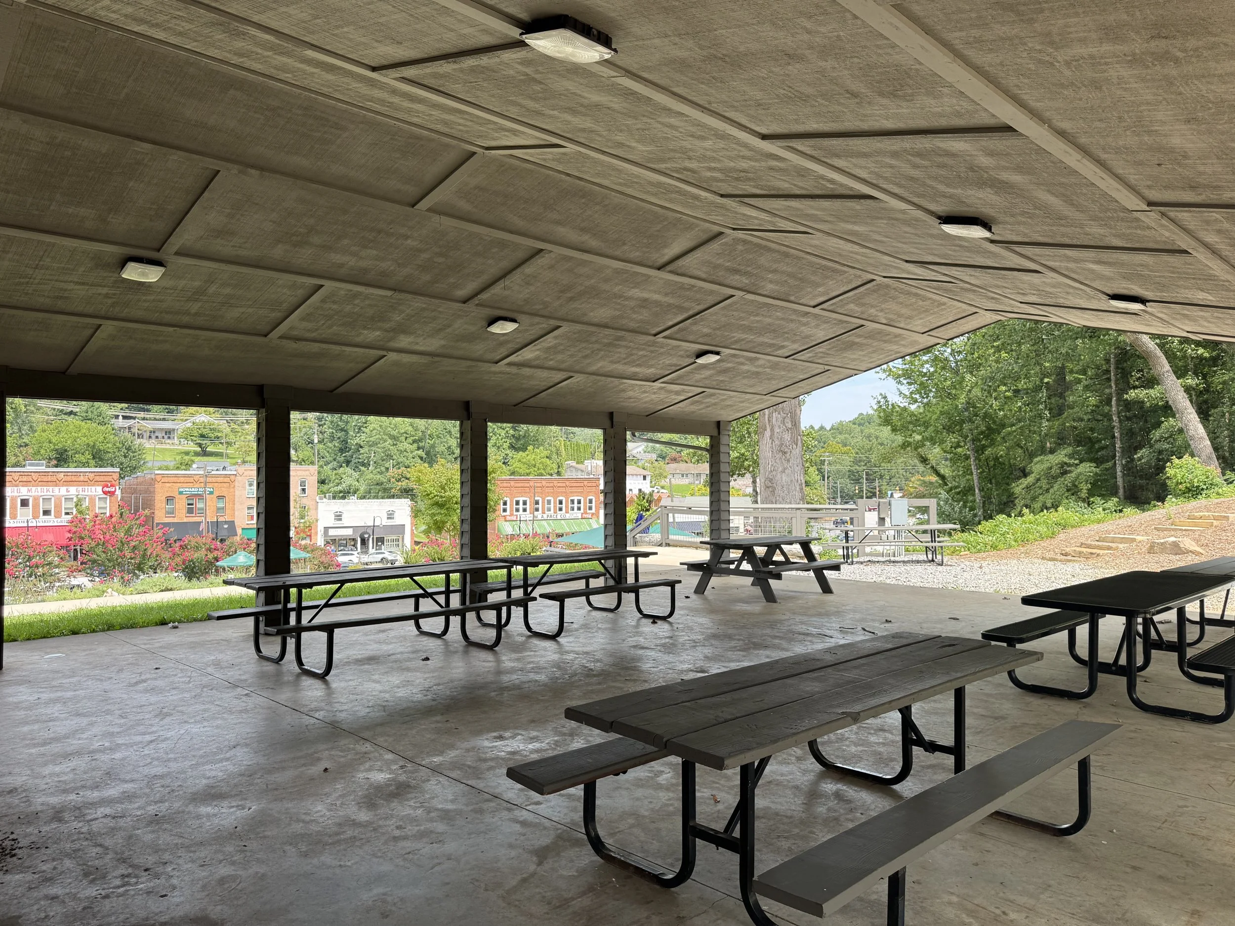 Outdoor covered area with picnic tables, overlooking a small town and green trees.