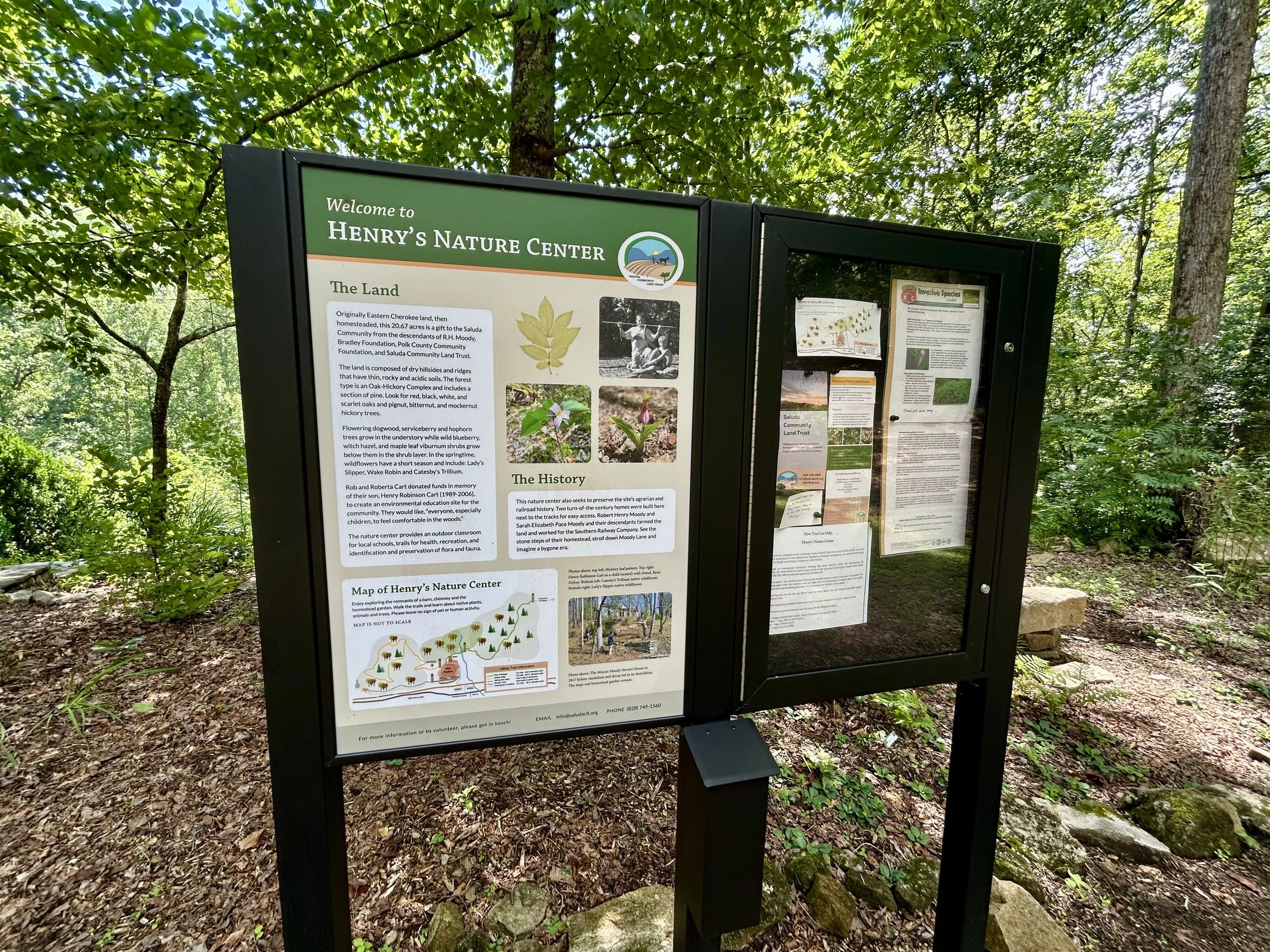 Outdoor informational signboard at Henry's Nature Center, situated in a wooded area with trees and greenery visible in the background.