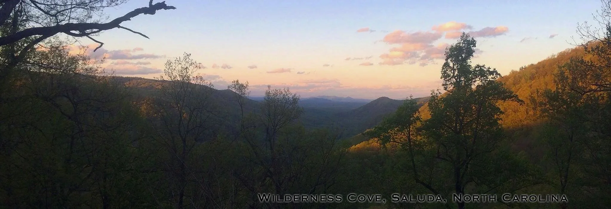 Sunset over rolling hills and mountains with scattered trees and a partly cloudy sky in Wilderness Cove, Saluda, North Carolina.