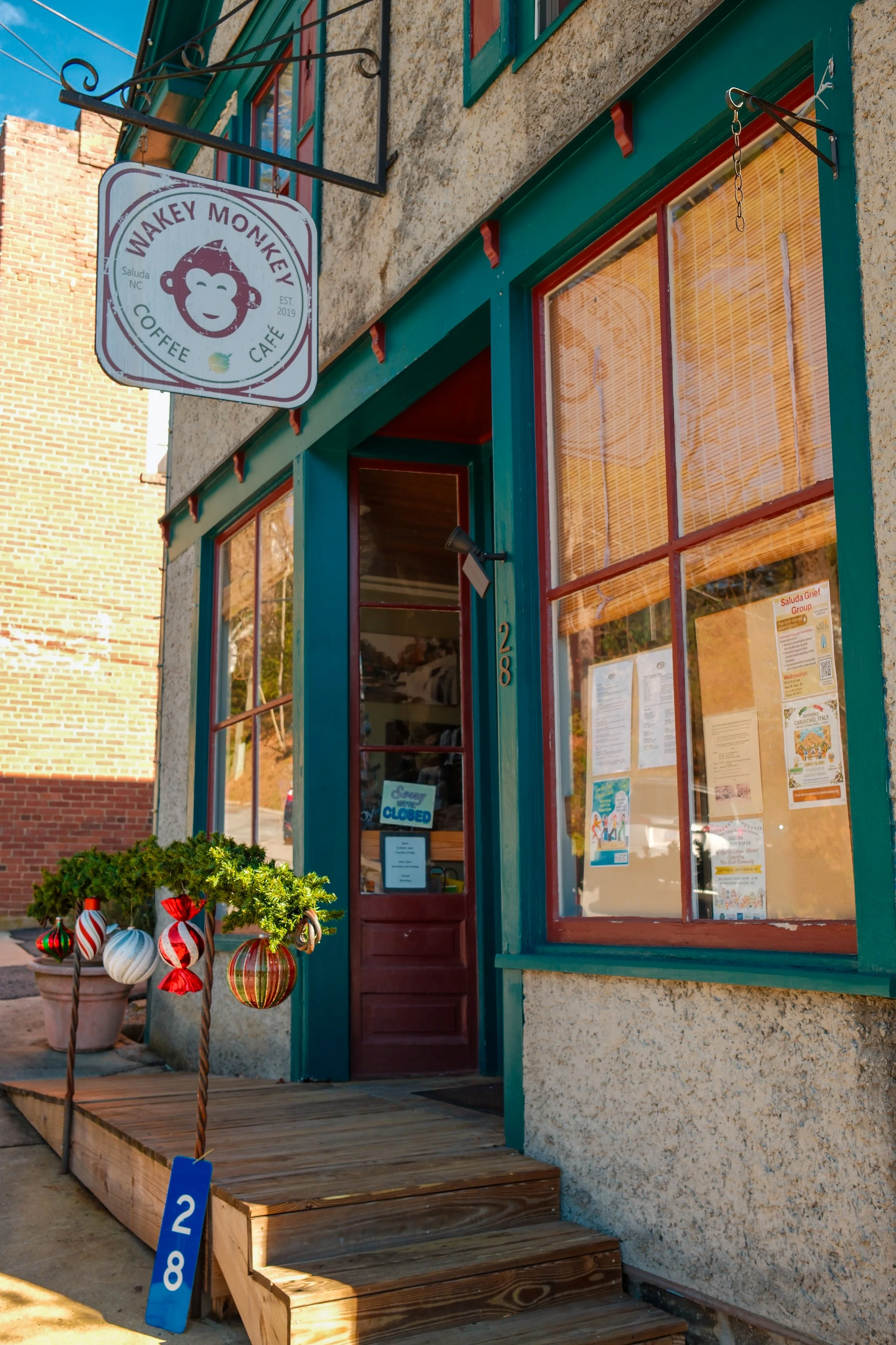 Exterior of a coffee shop with a colorful sign featuring a monkey face, a small wooden ramp, and festive holiday ornaments outside the entrance.