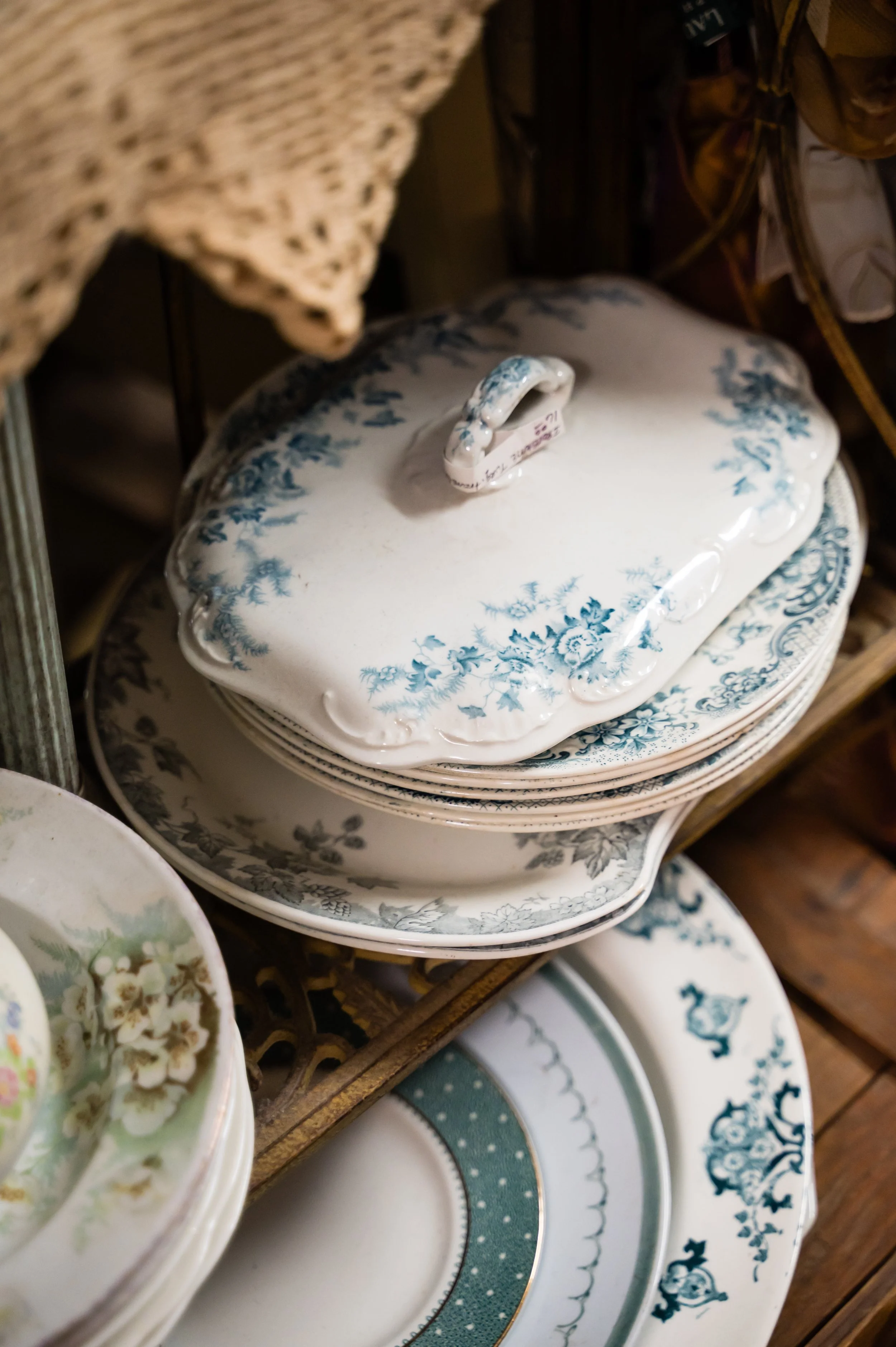 Stack of decorative porcelain dishes and plates with blue floral patterns and gold accents, displayed on a shelf.