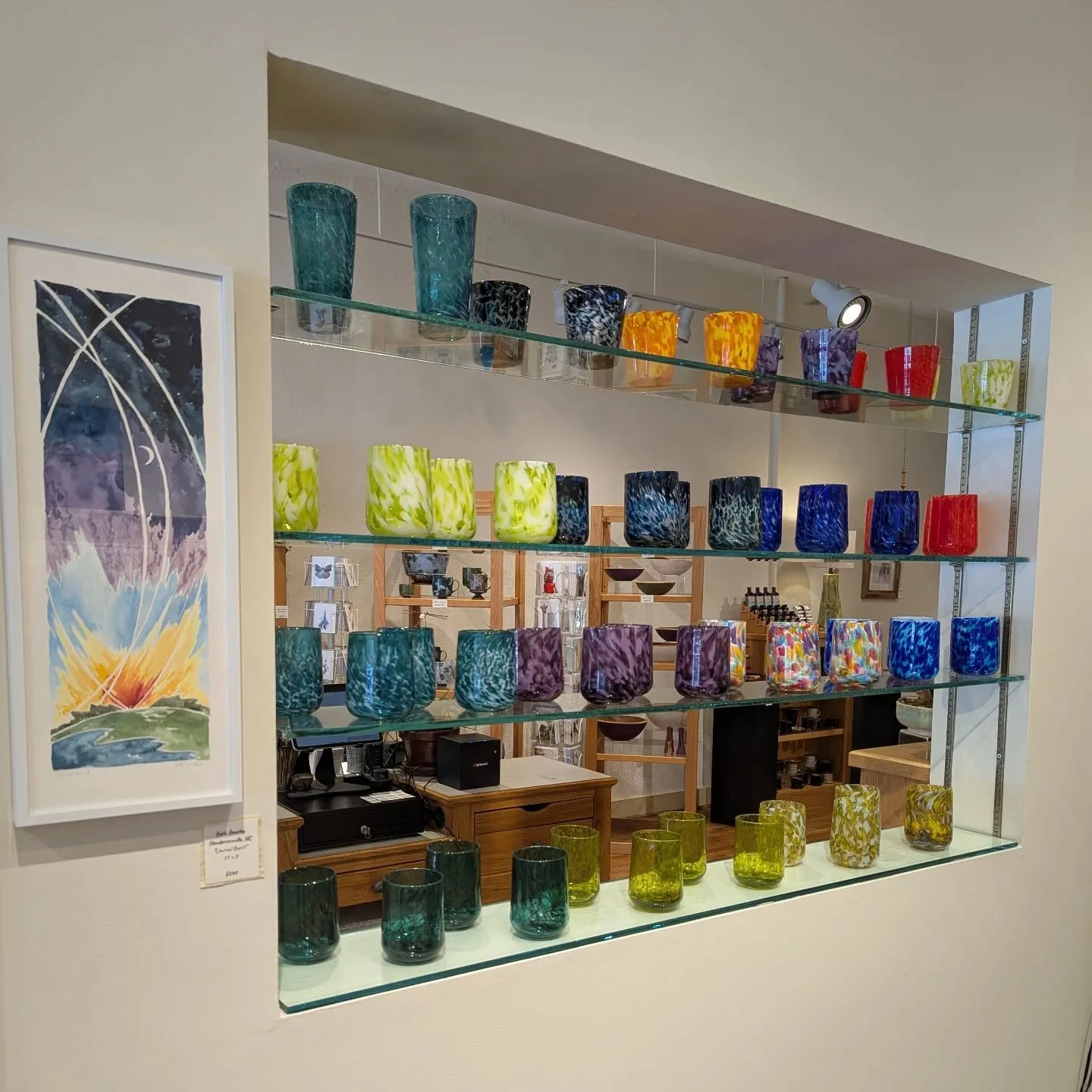 Display of colorful glass vases on glass shelves in an art gallery or shop.