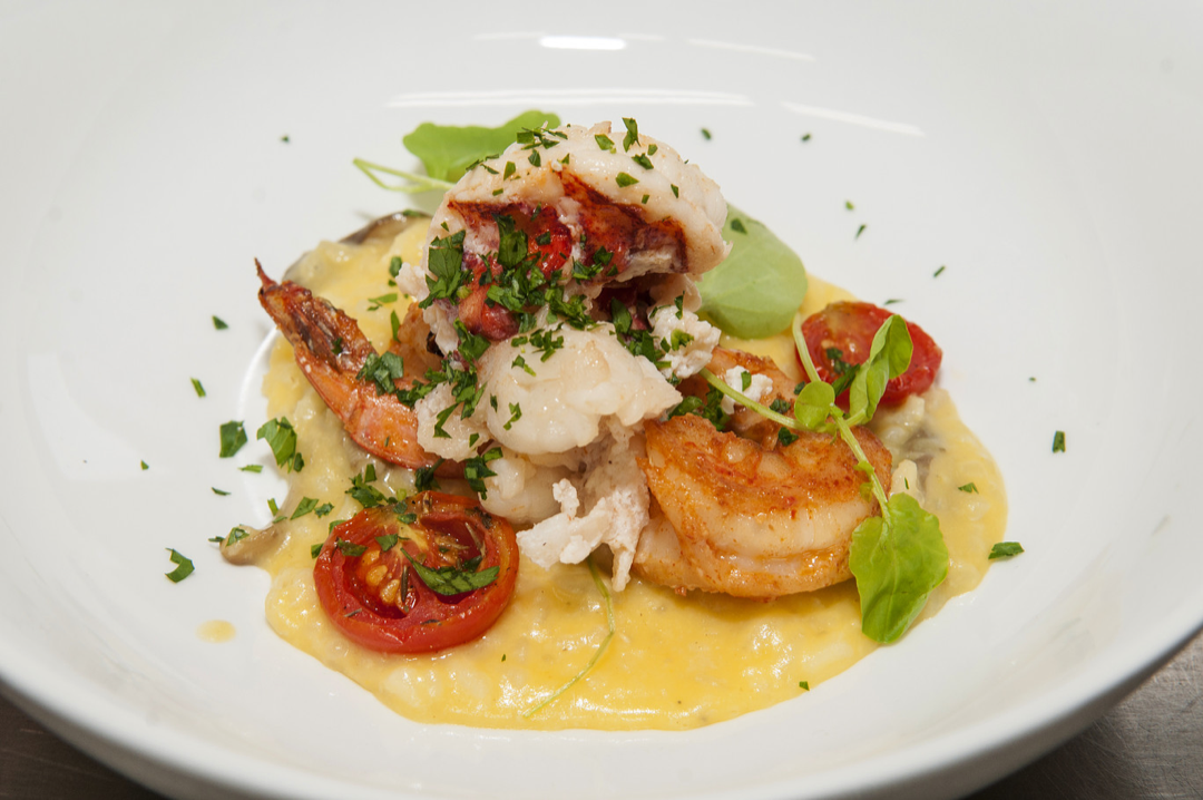 Lobster tail served on a bed of creamy yellow sauce with cherry tomatoes, greens, and herbs garnished on top.