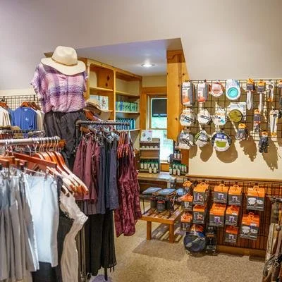 Clothing and accessories display in a retail store, including dresses, hats, and various kitchenware on wall hooks.