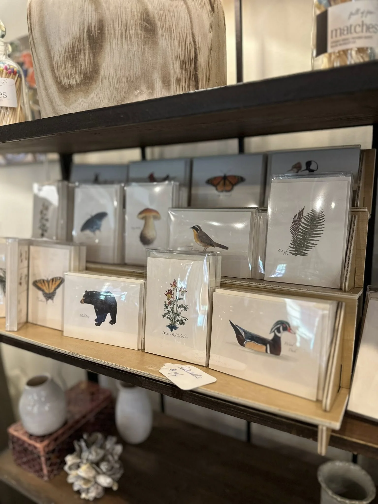 Display of butterfly, bird, and plant illustrations on greeting cards on a wooden shelf.
